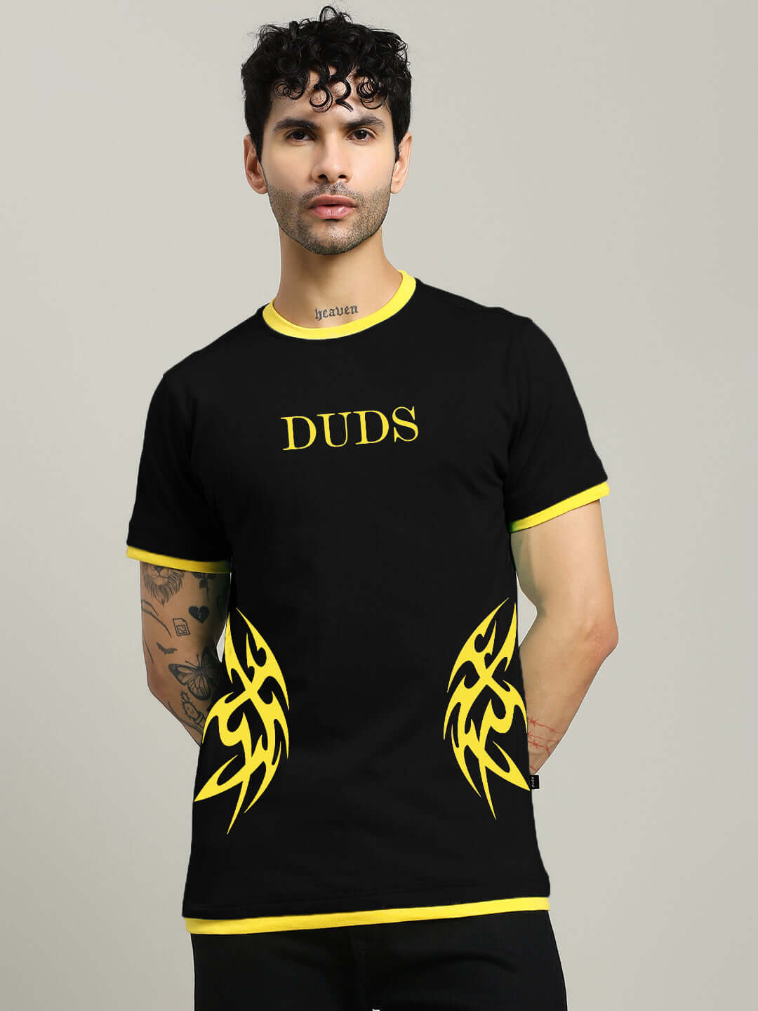 Man wearing a black t-shirt with yellow tribal patterns and 'DUDS' text, styled with curly hair, showcasing casual fashion.