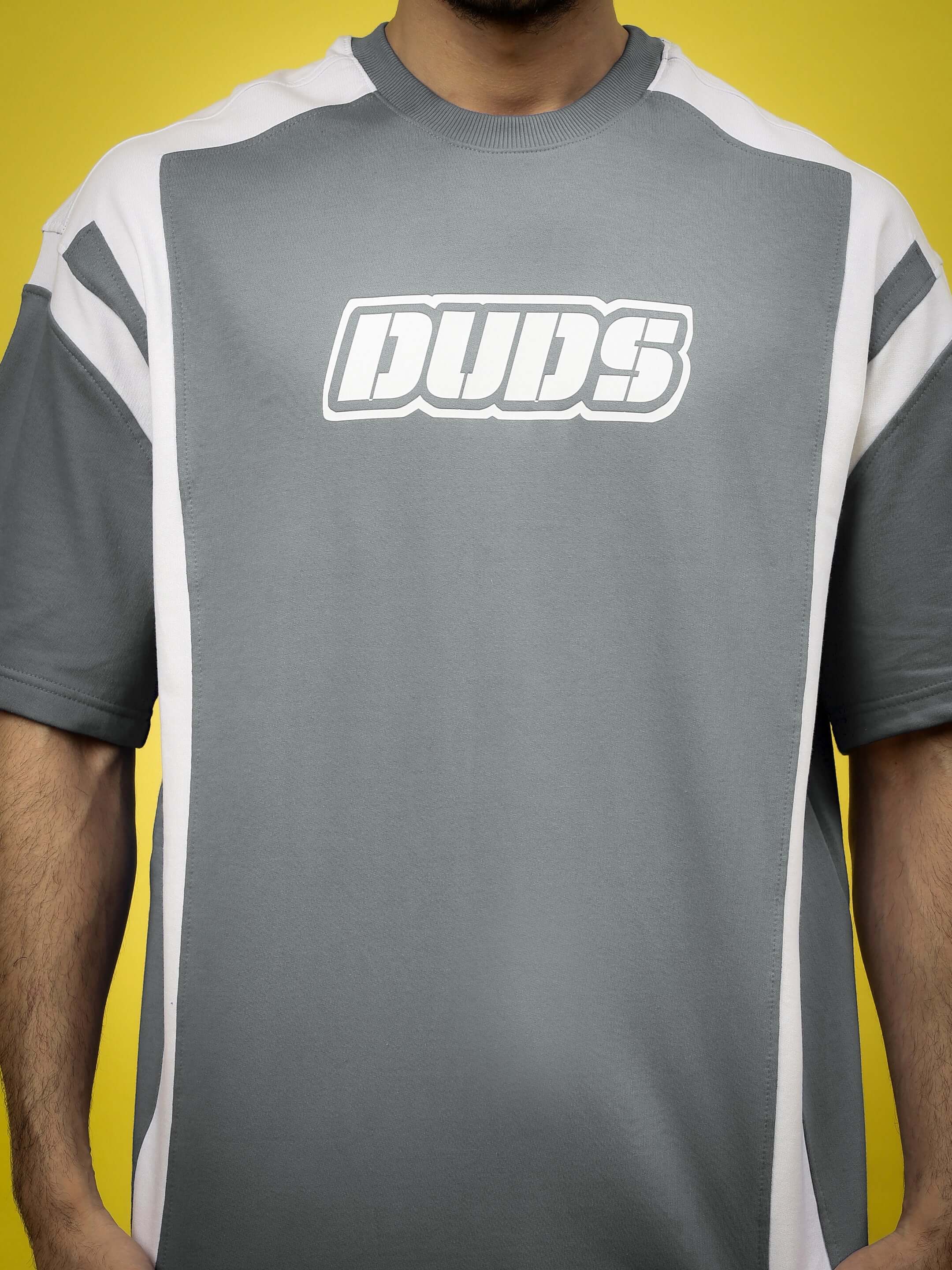 Person wearing NINJA STORM OVER-SIZED T-SHIRT GREY with bold graphic print, ideal for streetwear fashion, on a yellow background.