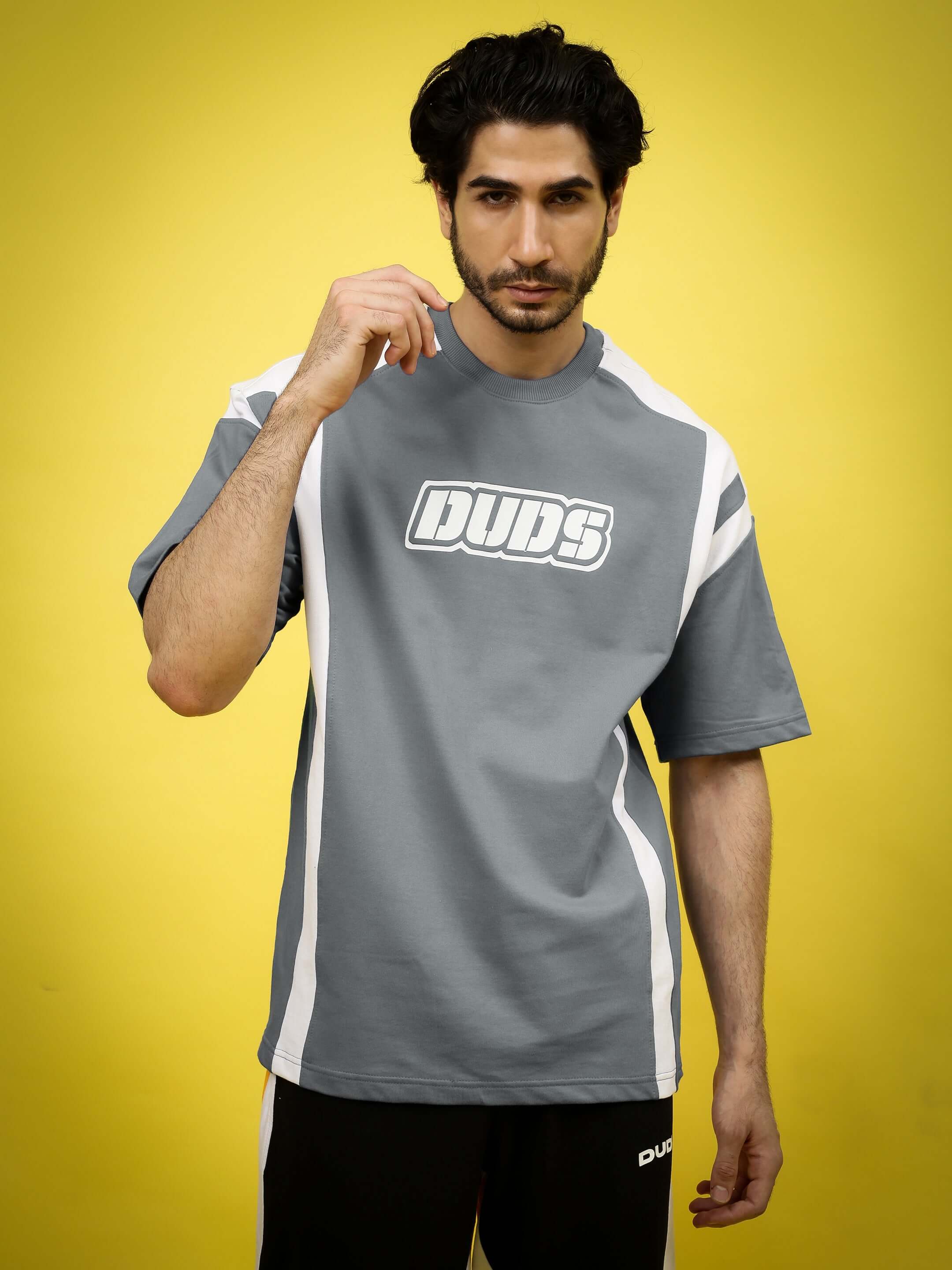 Model wearing grey oversized NINJA STORM T-shirt made of premium cotton blend, featuring white accents and logo, against yellow backdrop.