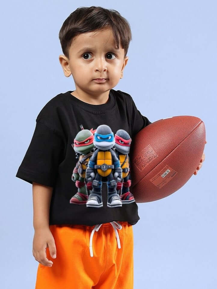 Child wearing NINJA TURTLES T-SHIRT FOR BOYS AND GIRLS BLACK holding a football.