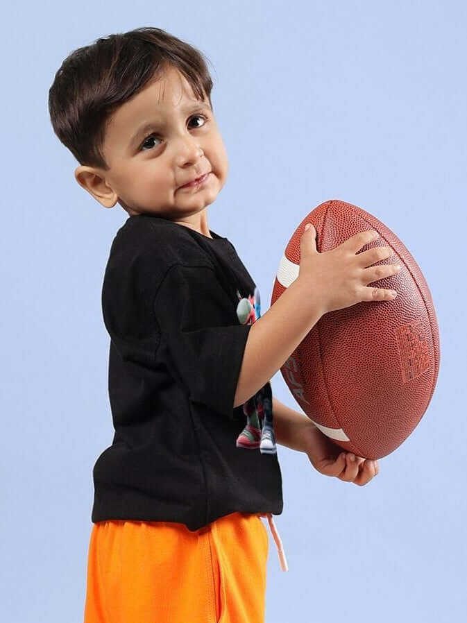 Child wearing NINJA TURTLES T-SHIRT FOR BOYS AND GIRLS BLACK holding a football, perfect for school or playdates.