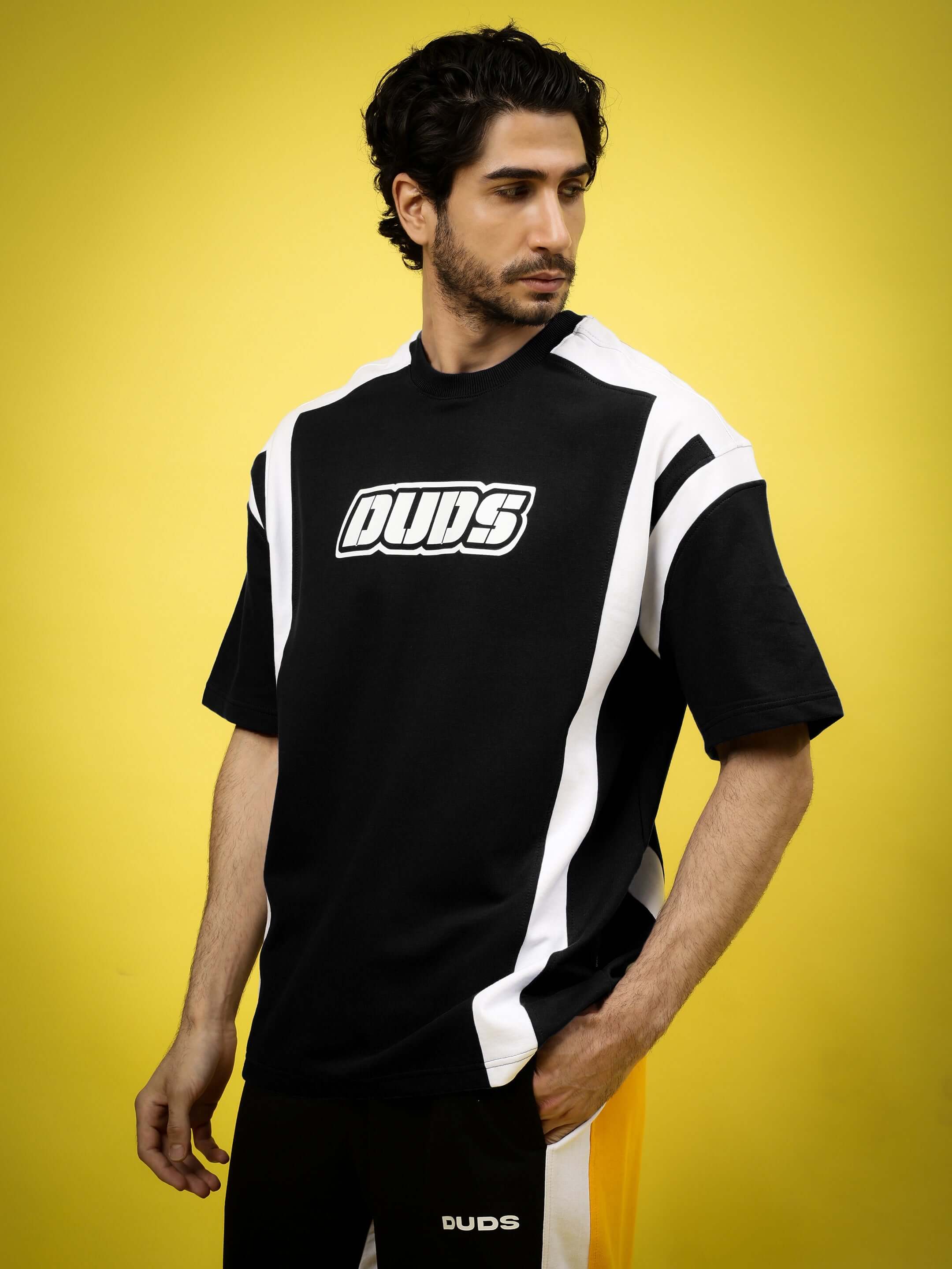 Man wearing black oversized T-shirt with white stripes, standing against a yellow background