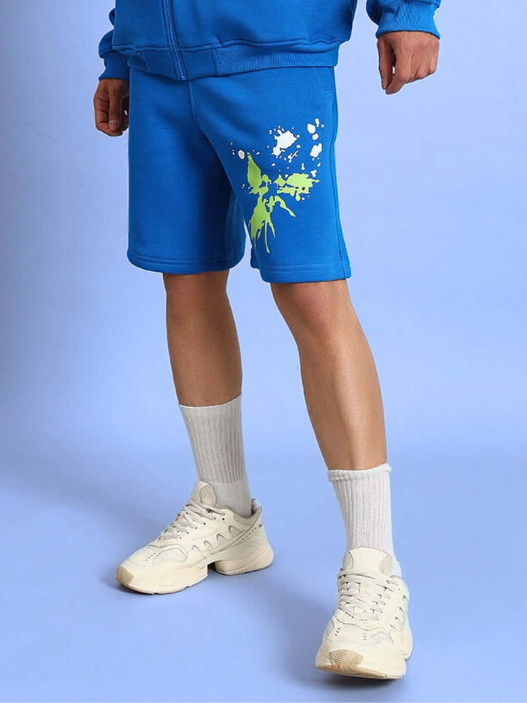 Person wearing NO DRAMA COTTON FLEECE SHORTS ROYAL BLUE with graffiti print, showcasing stylish streetwear fashion.