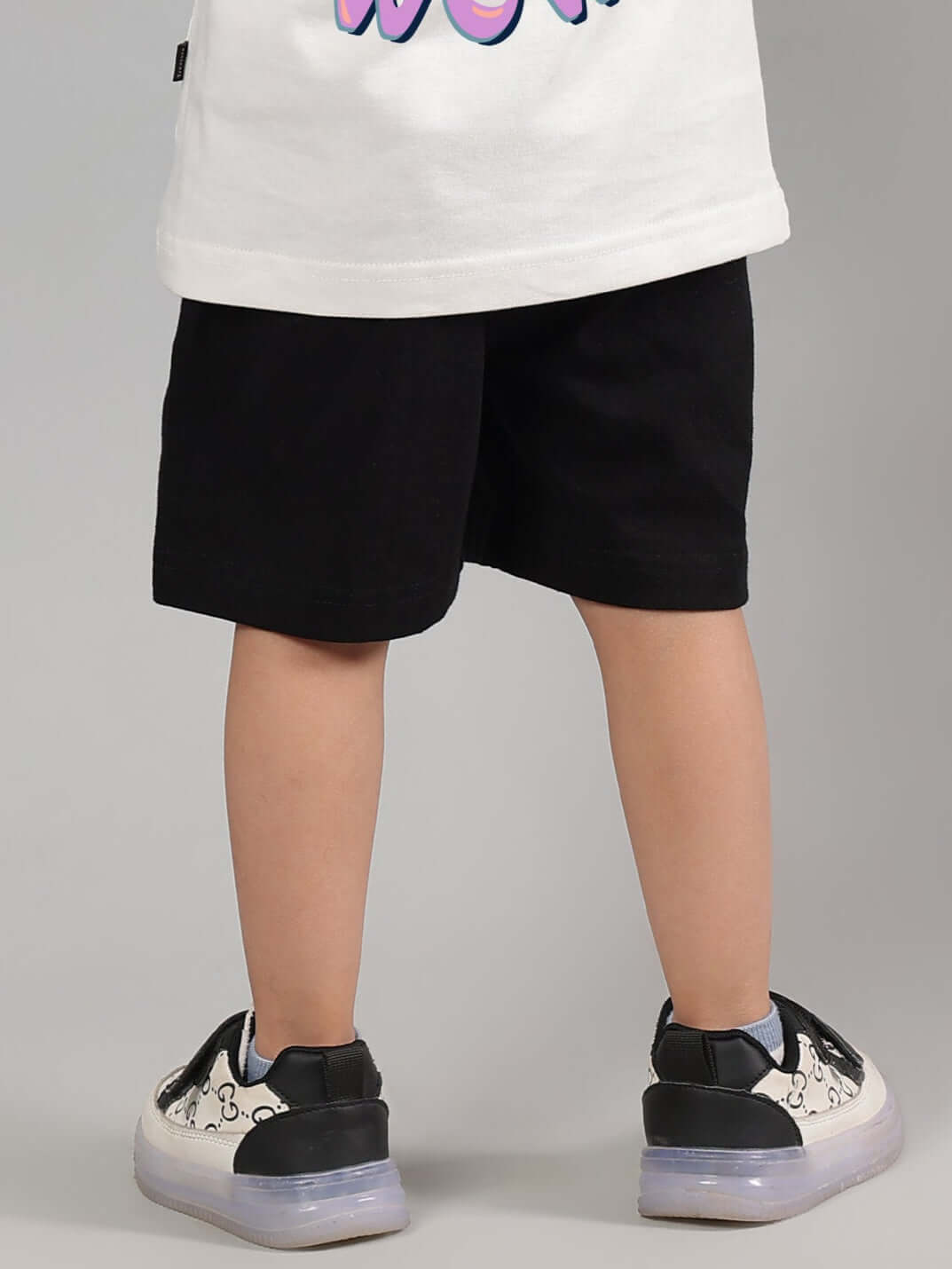 Child wearing black NO POS shorts showcasing back view, made-to-order by DUDS with customizable fit options. Casual and stylish kidswear.