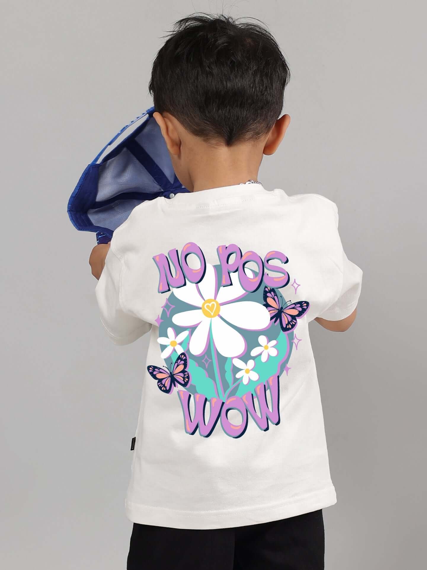 Child wearing a NO POS WOW off-white T-shirt with floral and butterfly design on the back.