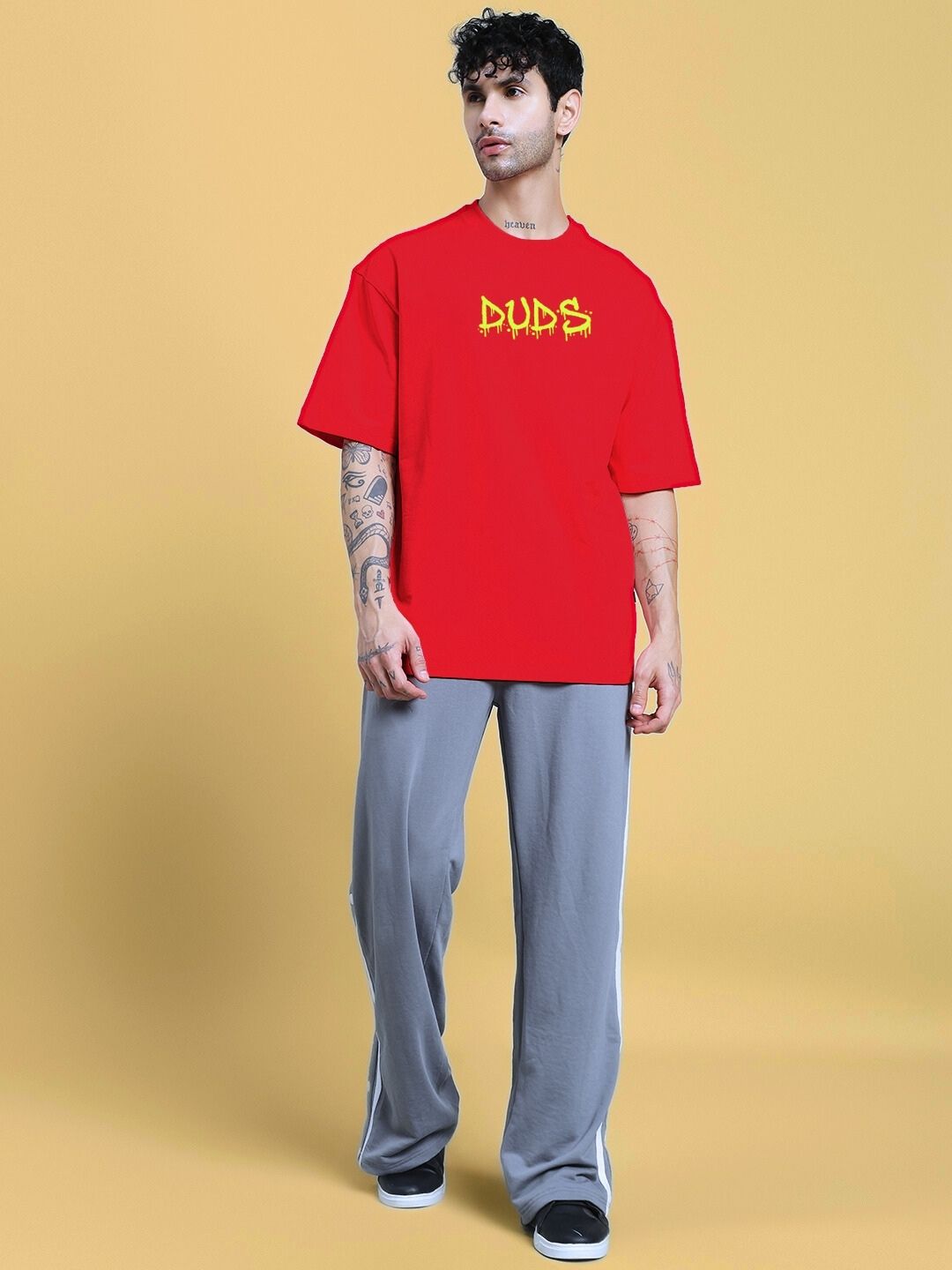 Man wearing NO WAR OVER-SIZED T-SHIRT IN RED and gray pants, standing against a yellow background.