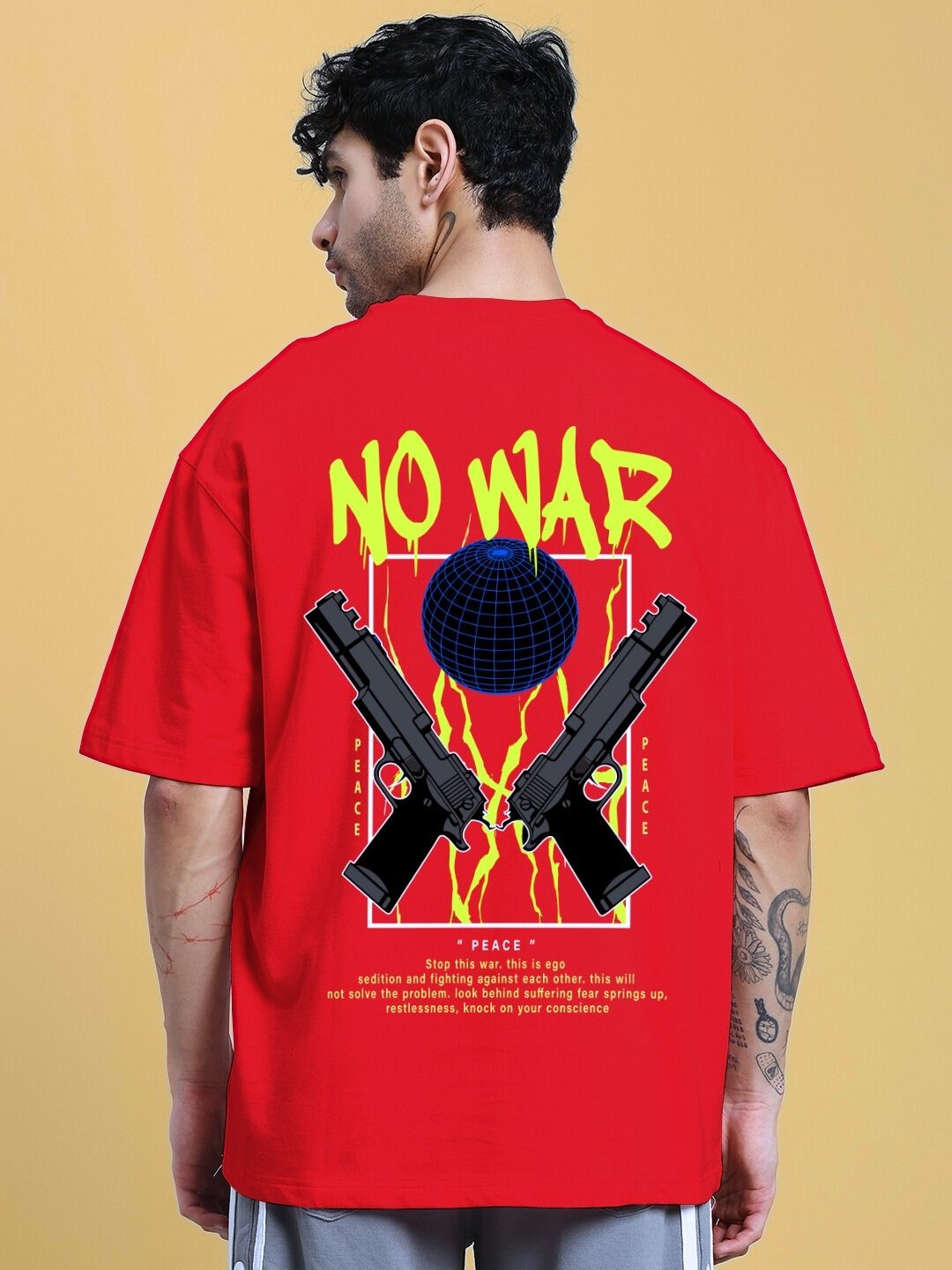 Back view of a man wearing NO WAR OVER-SIZED T-SHIRT IN RED with graphic design featuring peace symbol, guns, and globe.