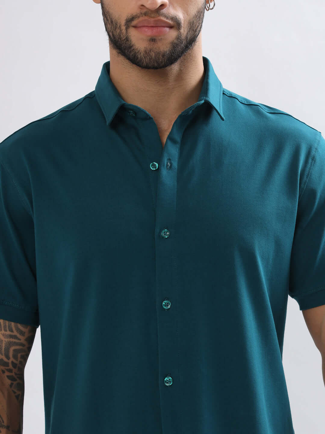 Man wearing a NOIR teal blue shirt with half sleeves, featuring 4-way stretch, wrinkle-free cotton Lycra, curved hem, and slim fit.