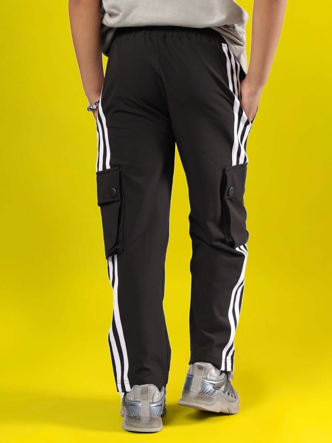 Child wearing NOVA Jogger for Boys & Girls in black, featuring sporty white stripes and cargo pockets, against a yellow background.