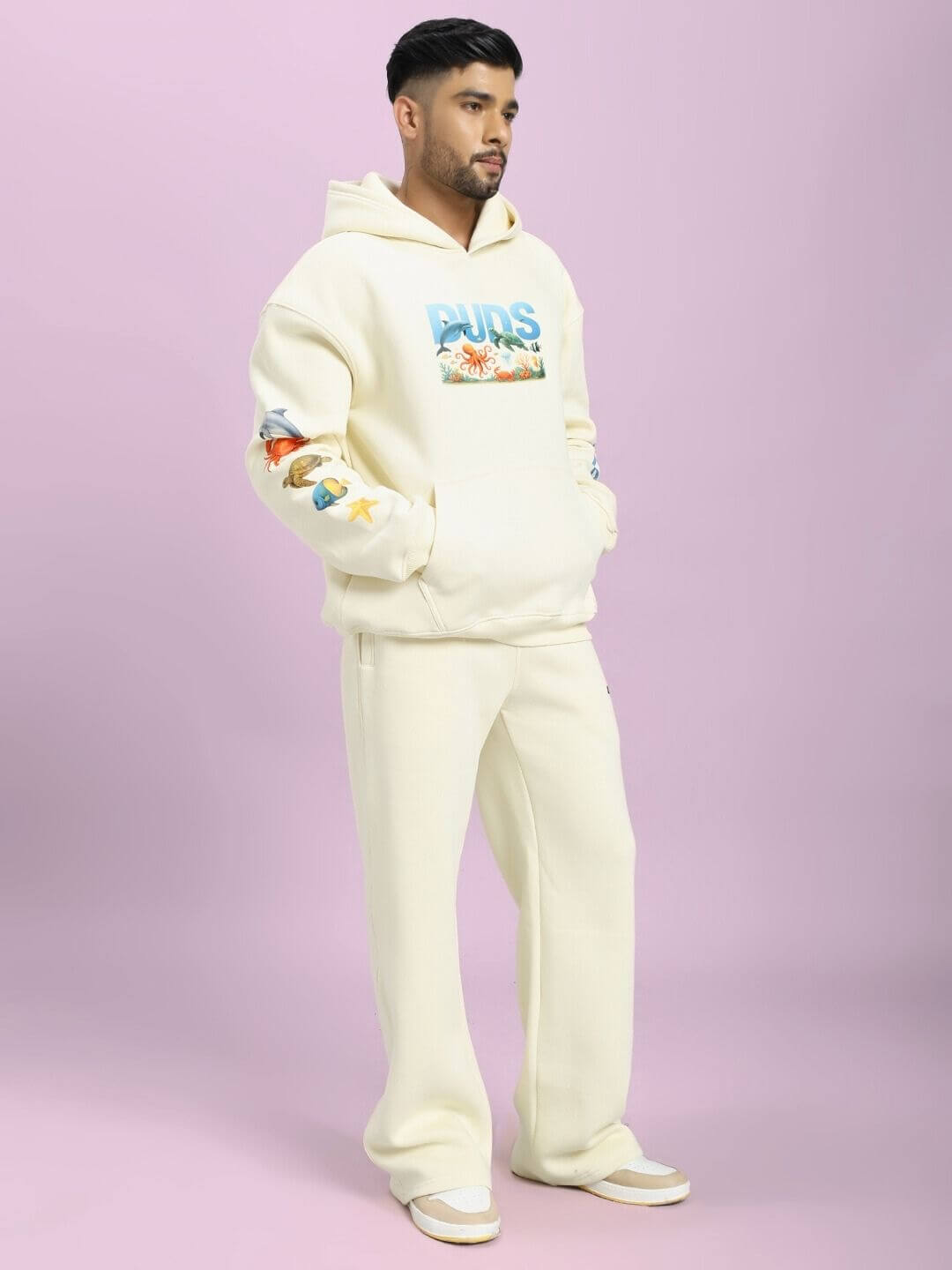 Person wearing OCEAN BUDDIES FLEECE CO-ORD SET OFF-WHITE with sea-inspired graphics against a purple background.