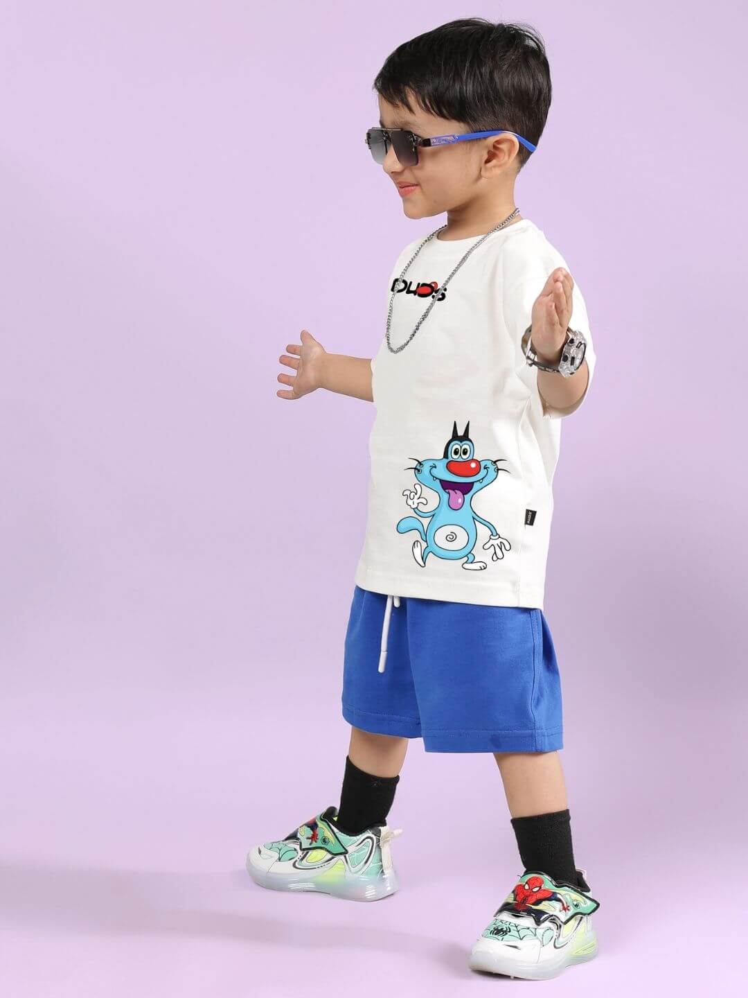 Boy wearing Oggy printed co-ord set with off-white T-shirt and blue shorts, featuring a fun cartoon design and sunglasses.