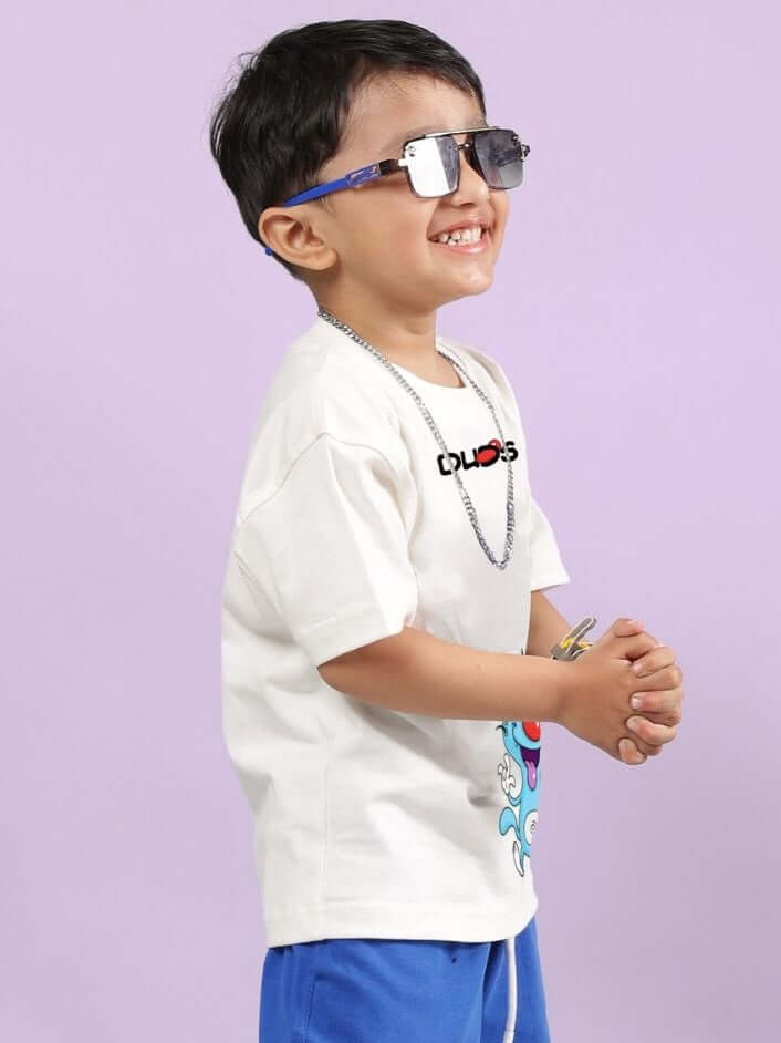 Child wearing OGGY PRINTED T-SHIRT FOR BOYS AND GIRLS OFF WHITE with sunglasses, smiling and posing against a purple background.