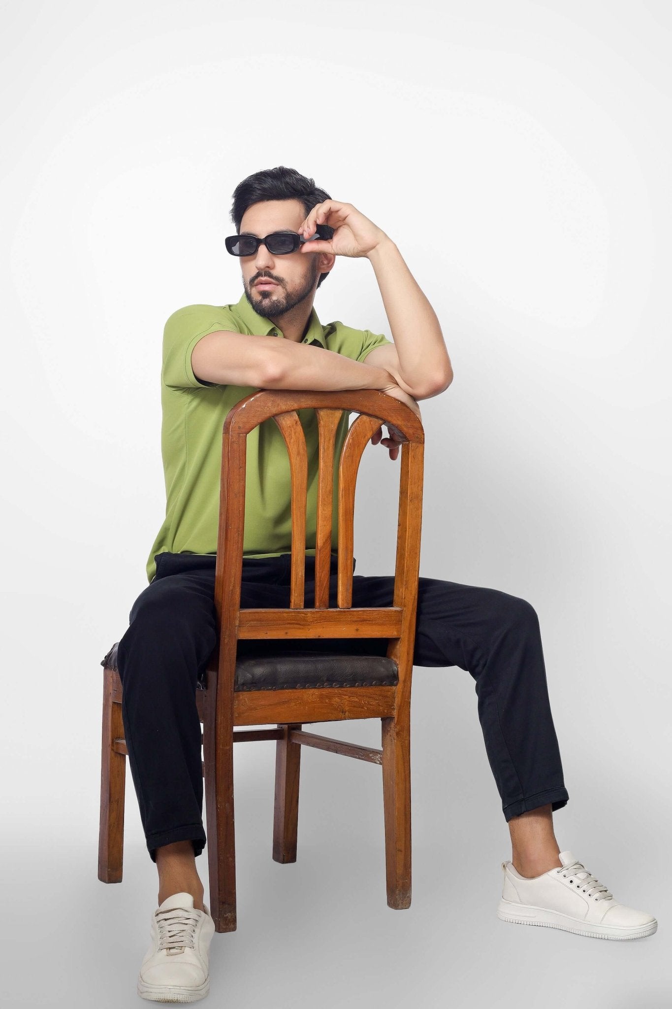 Man wearing DUDS OLIVE GREEN POLO NECK T-SHIRT sitting stylishly on a wooden chair, showcasing casual elegance and comfort.