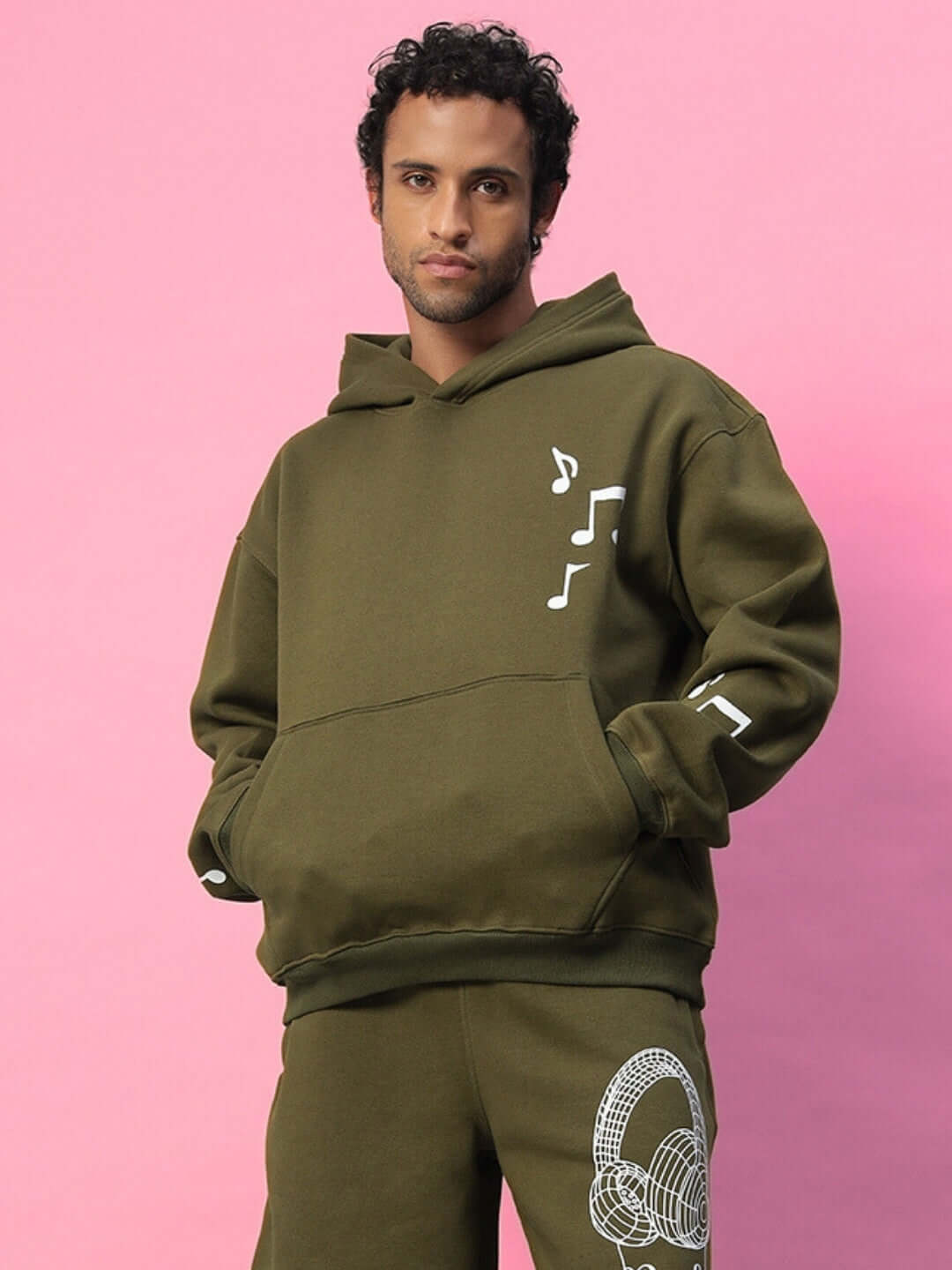 OPERA FLEECE HOODIE OLIVE GREEN modeled against a pink background, showcasing its stylish design and tailored fit.