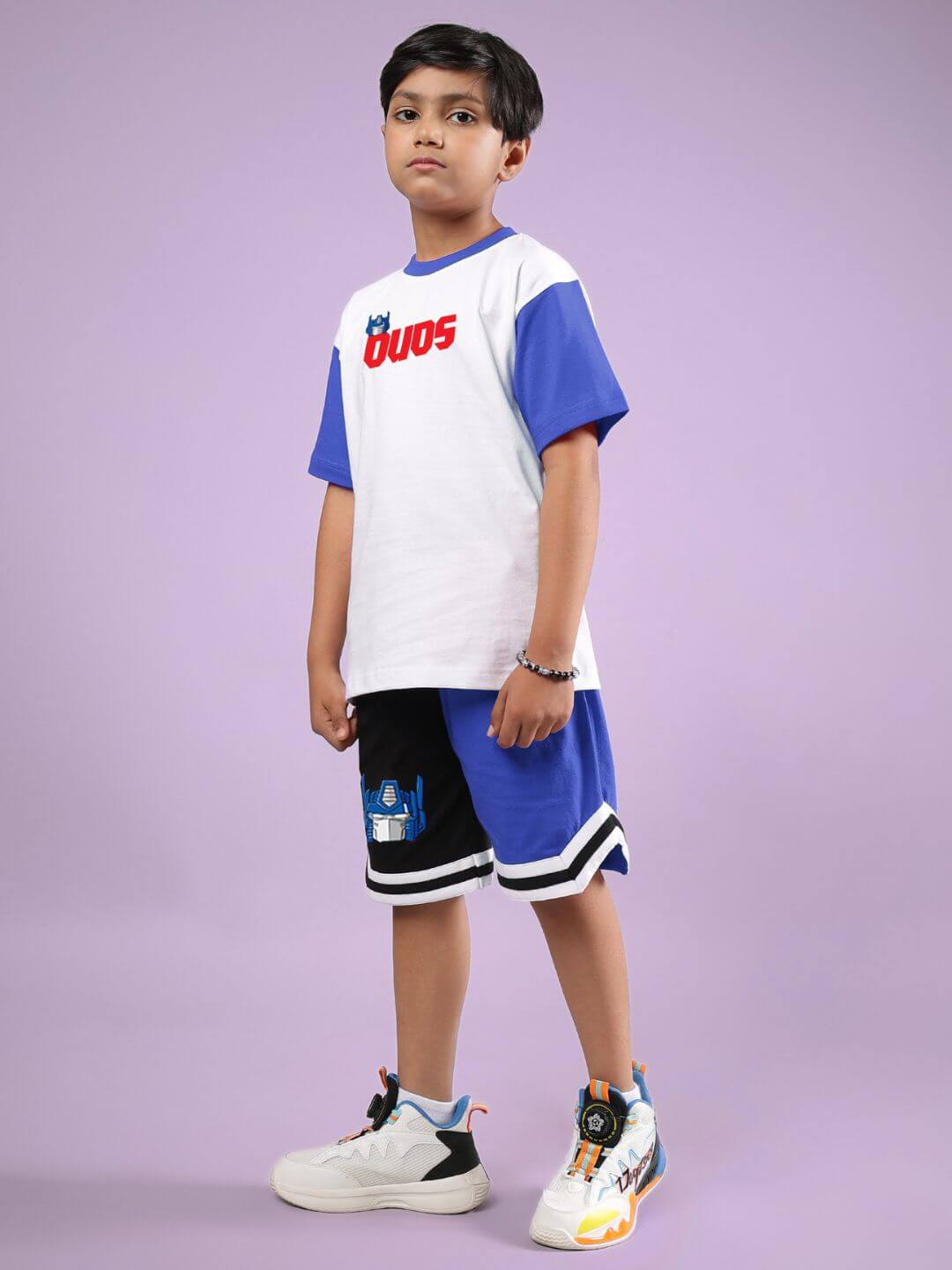 Young boy wearing the OPTIMUS PRIME CO-ORD FOR BOYS & GIRLS WHITE BLUE, featuring a white and blue design, standing against a purple background.