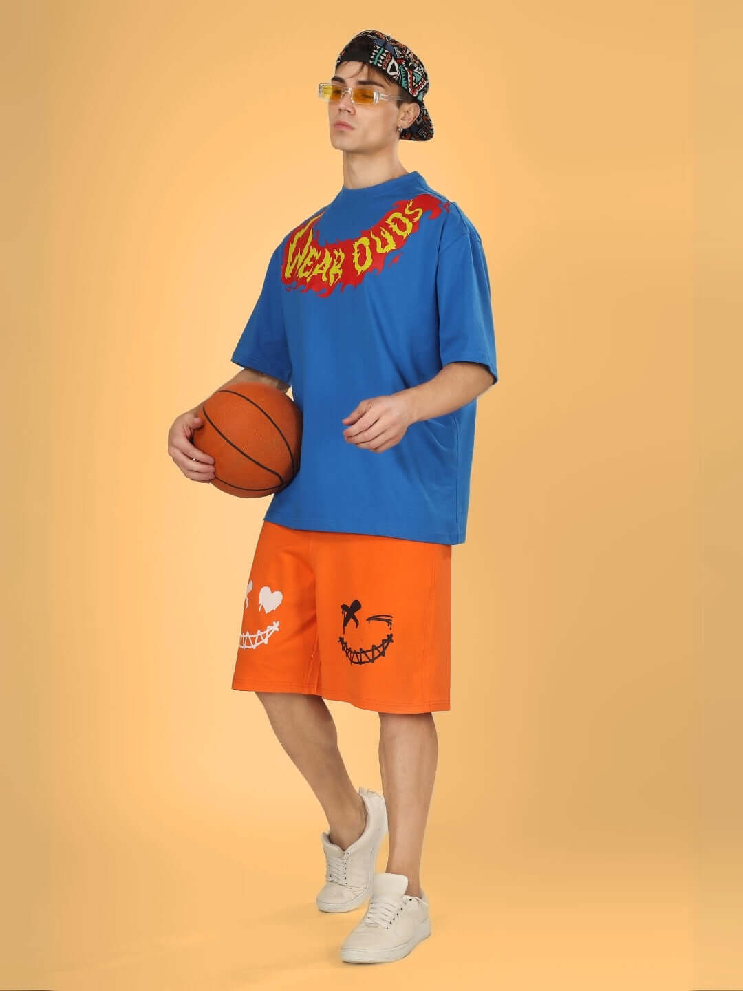 Model wearing Evil Smile regular fit orange shorts, holding a basketball. Features playful design graphics. Custom fit available.