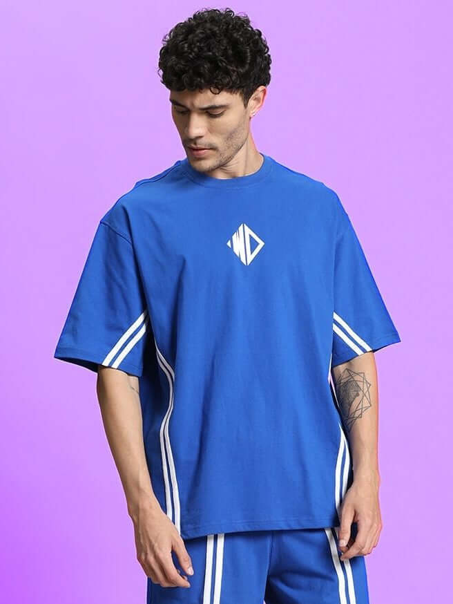Man wearing OUTLOOK OVER-SIZED T-SHIRT ROYAL BLUE, showing relaxed fit and vibrant color against a purple background.