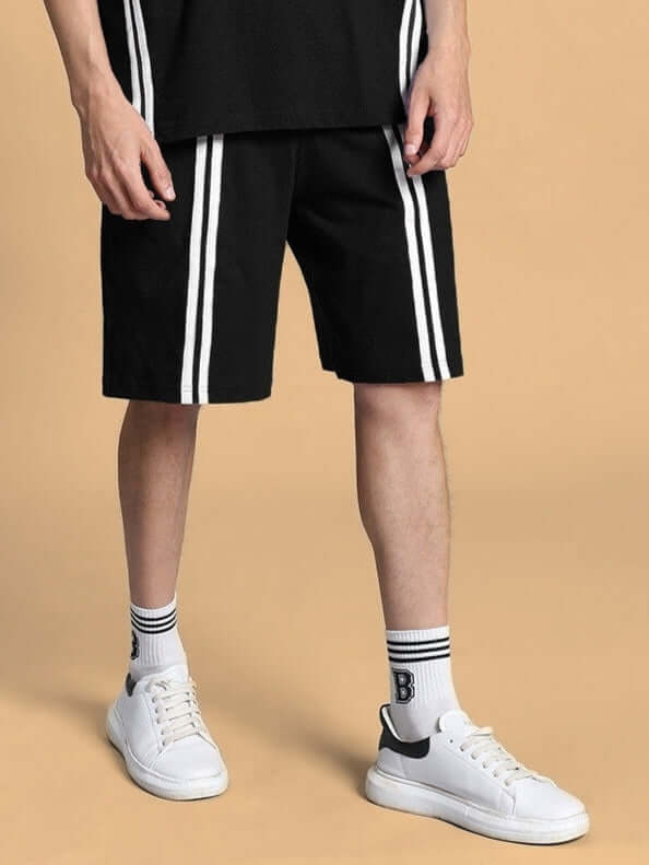 Man wearing OUTLOOK REGULAR FIT SHORTS BLACK with white stripes and sneakers.