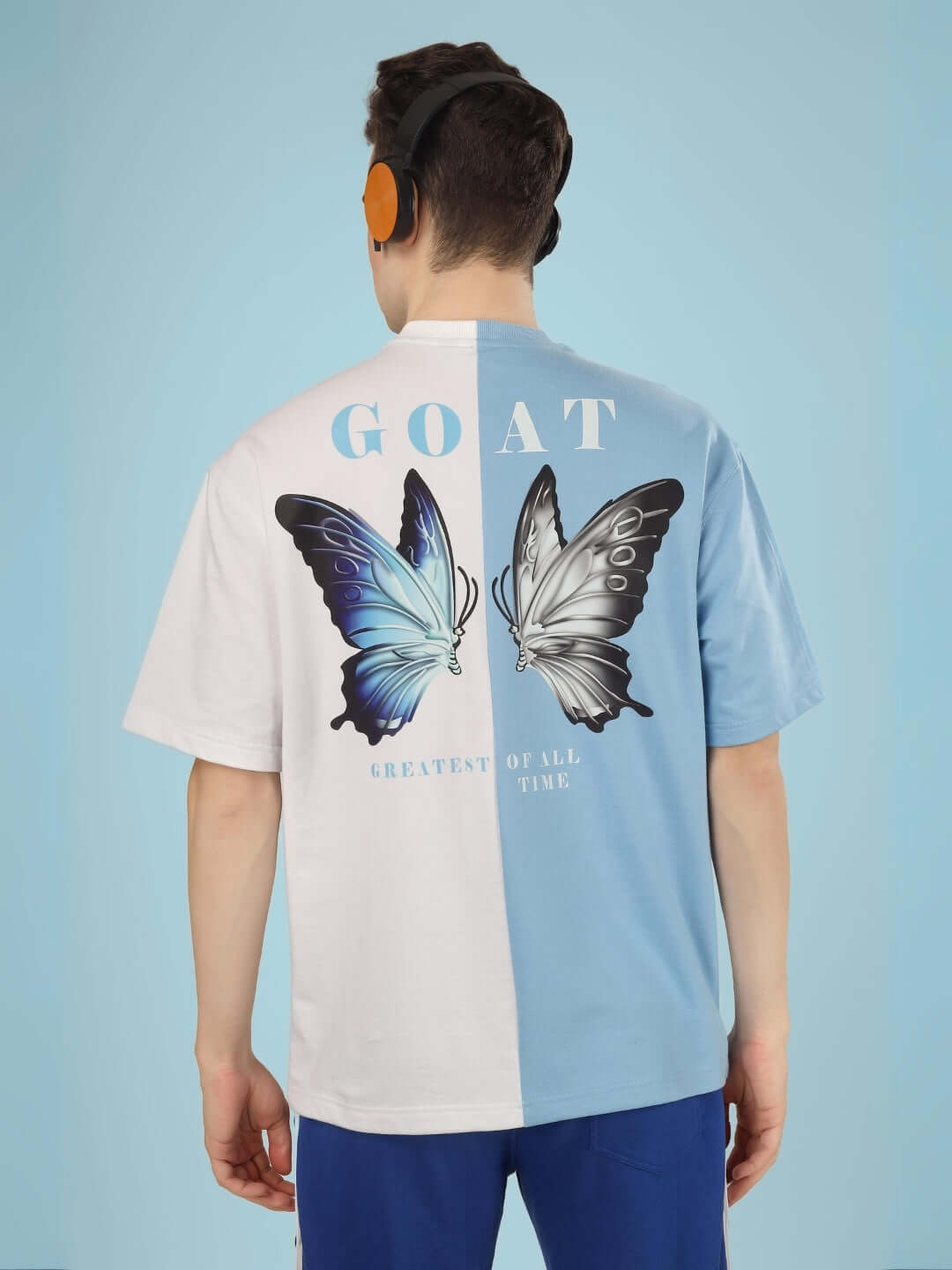 Man wearing a G.O.A.T oversized t-shirt in sky blue and white, featuring a butterfly graphic. Premium cotton French terry material from India.