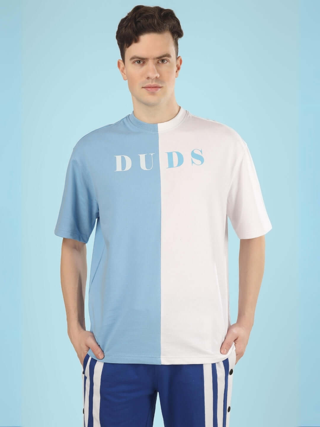 Man wearing a G.O.A.T oversized T-shirt in sky blue and white, made from premium cotton French terry, styled with blue striped pants.