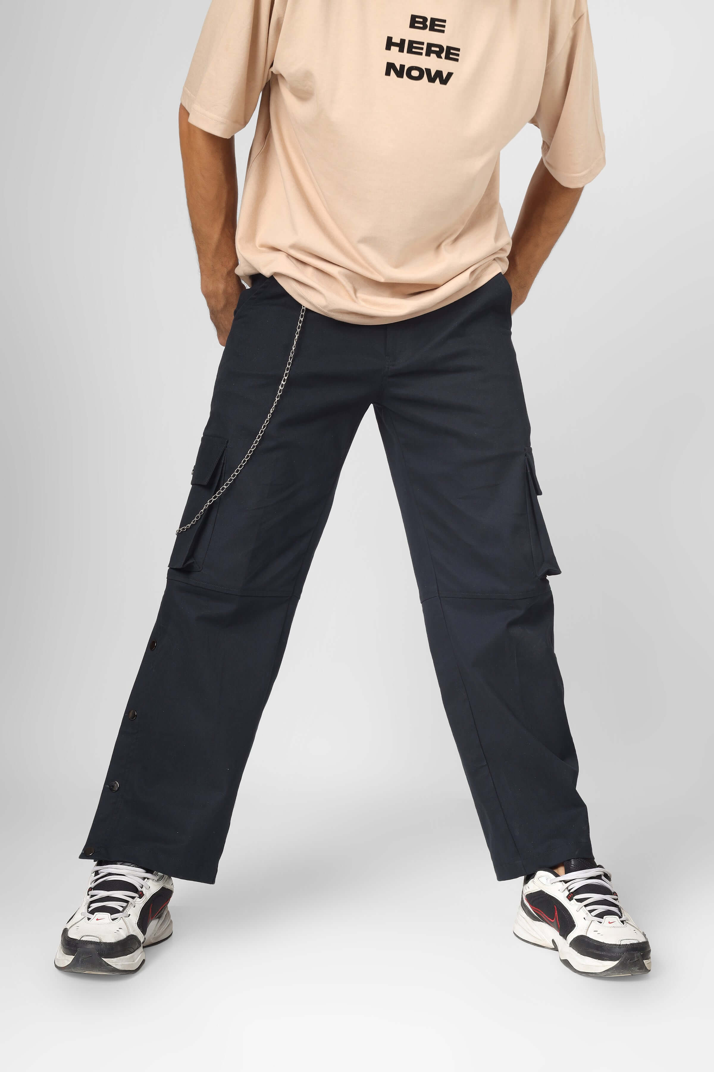 Person wearing Oxford blue cargo pants with six pockets and a chain accessory, paired with white sneakers and a casual beige t-shirt.