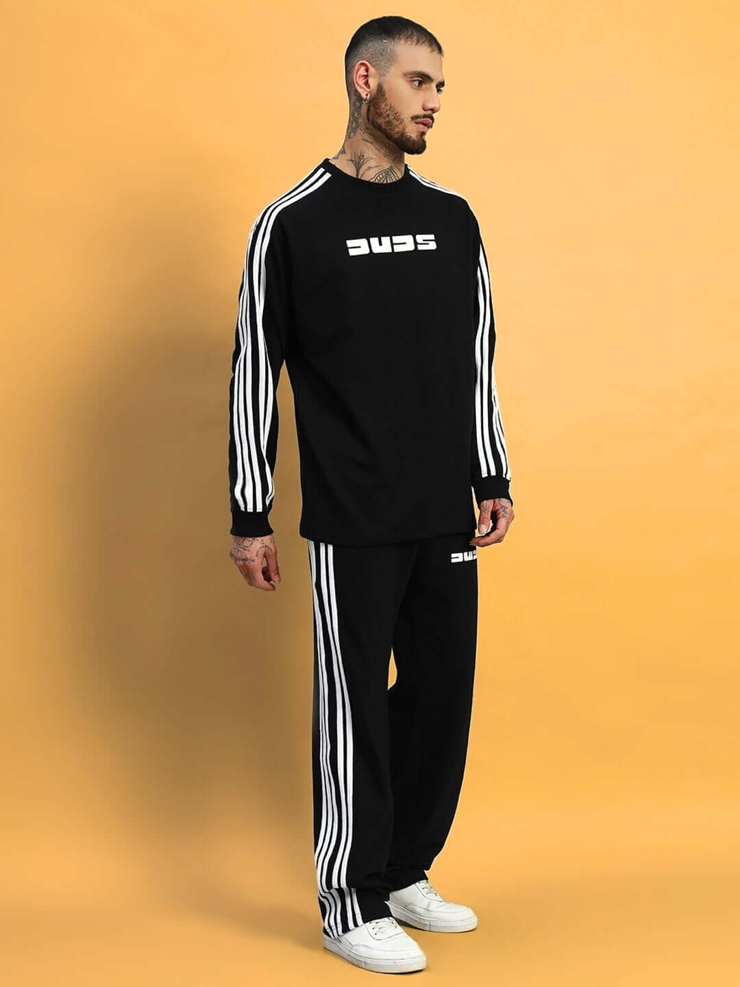 Man wearing PARKA OVERSIZED CO-ORD SET BLACK with white sneakers against a yellow background, highlighting its relaxed comfort and style.