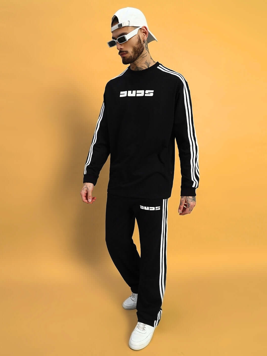 Man wearing oversized black parka co-ord set with white stripes, featuring relaxed fit joggers and branded top against a yellow background.