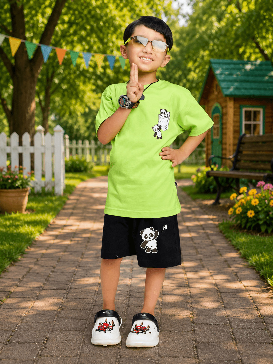 PEEK-A-PANDA COOL SHORTS FOR BOYS GIRLS BLACK worn by a smiling boy in a vibrant green shirt, posing outdoors.
