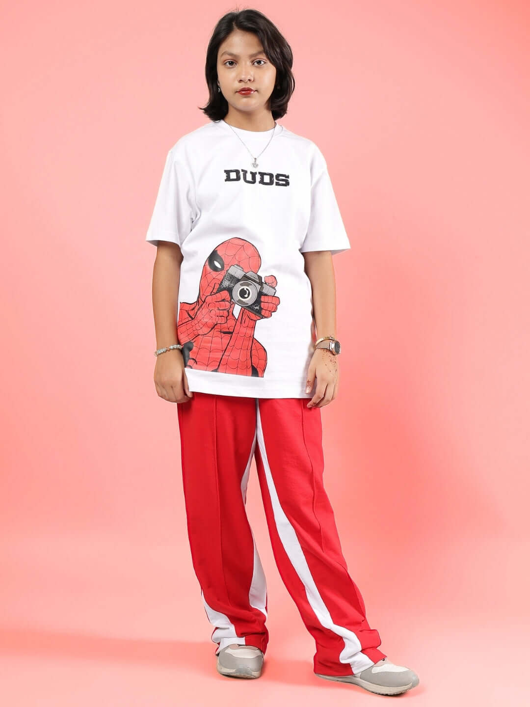 Child wearing PETER CO-ORD FOR BOYS & GIRLS WHITE-RED by DUDS, featuring graphic print shirt and red pants against pink background.