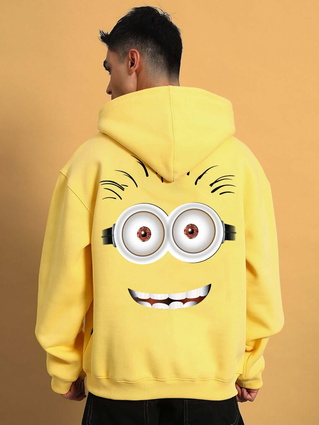 Person wearing PHIL MINION OVERSIZED FLEECE HOODIE YELLOW with Minion character design on the back.