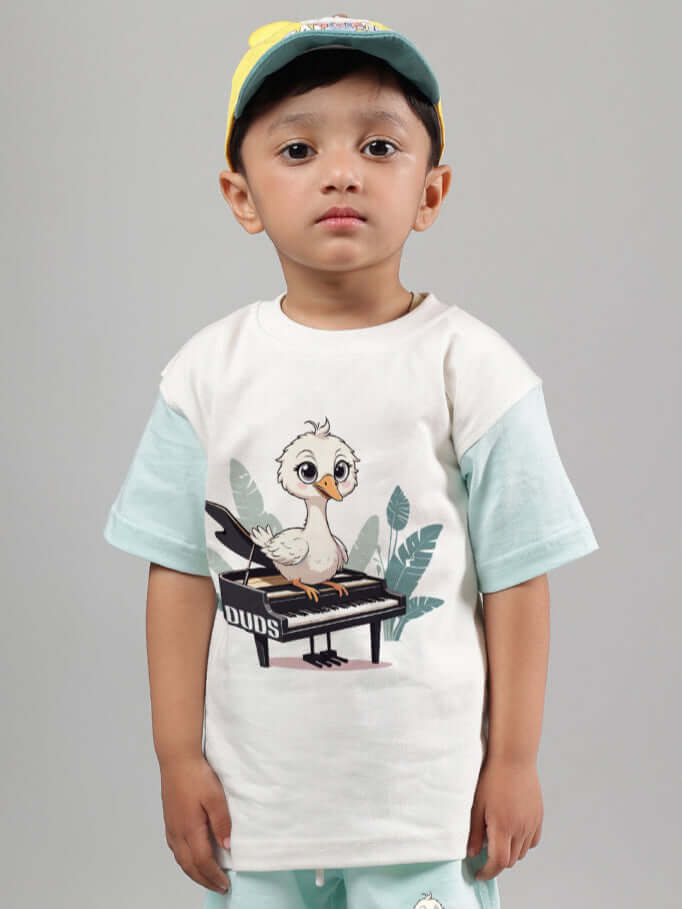 Child wearing off-white and blue Piano Bird T-shirt for boys and girls by DUDS, featuring a cute bird on piano print.