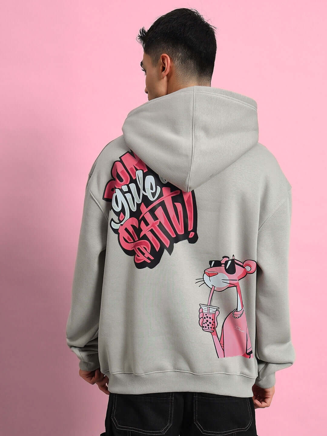 Back view of model wearing PINK PANTHER FLEECE OVERSIZED HOODIE GREY with Pink Panther graphic and lettering, against a pink background.