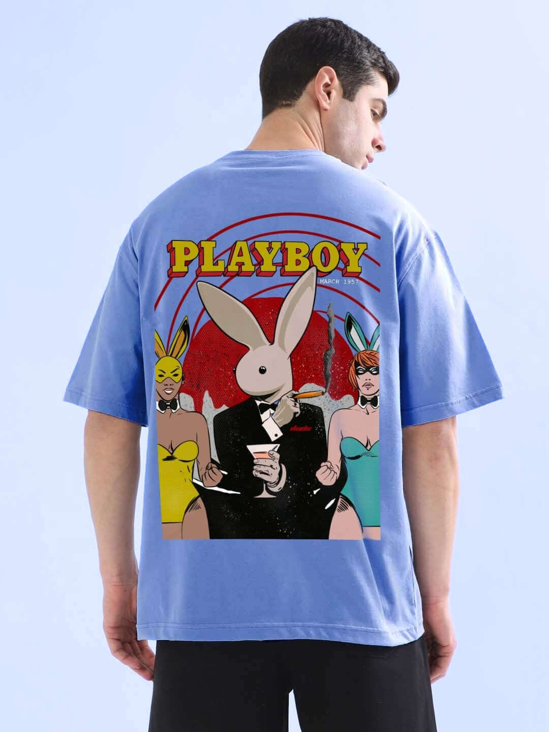 Man wearing a Playboy oversized t-shirt in cobalt blue featuring a graphic of a rabbit and models, made from premium cotton fabric.