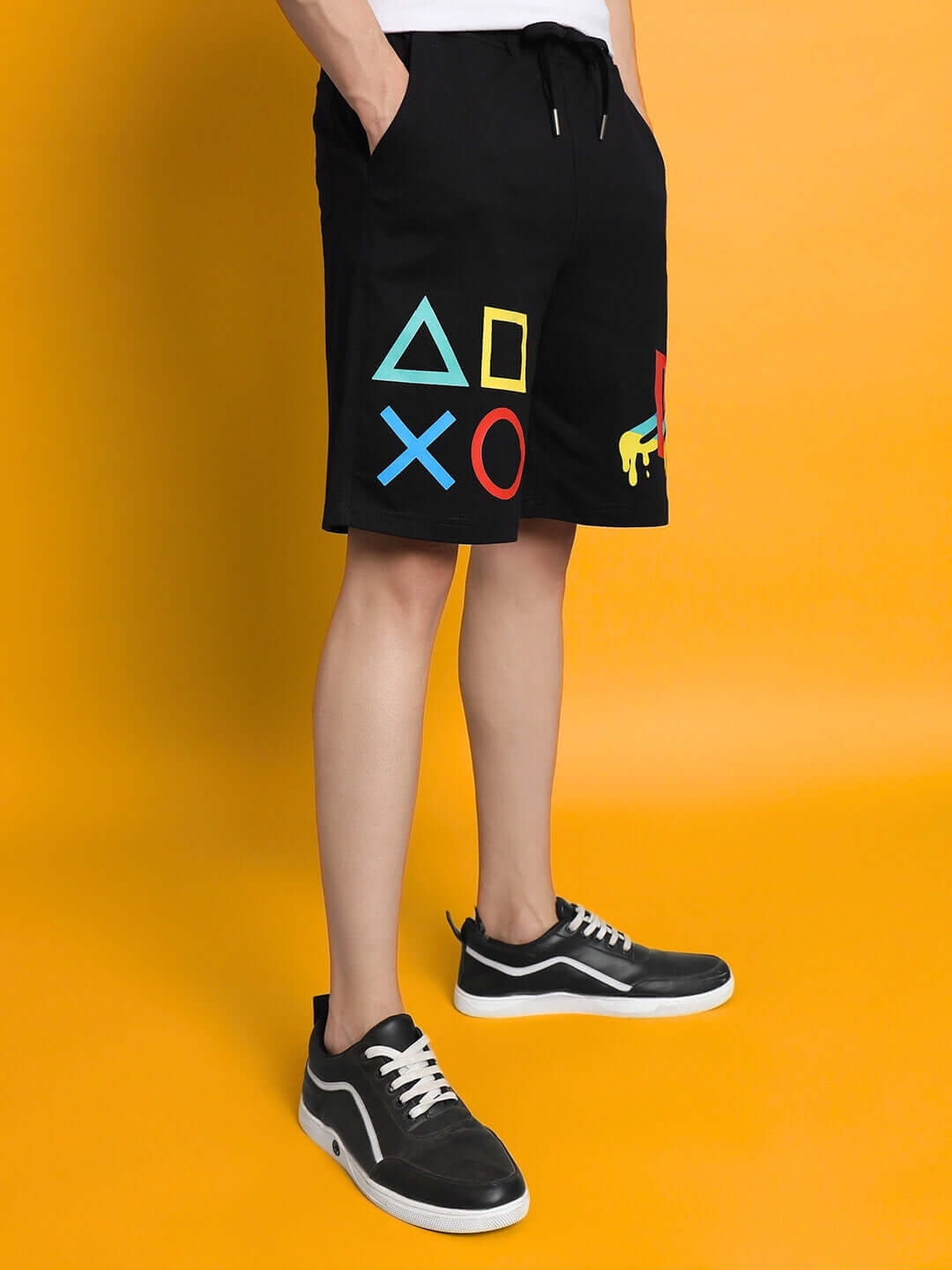 Black PlayStation regular fit shorts featuring iconic symbols, customizable fit, shown styled with casual black sneakers on yellow backdrop.