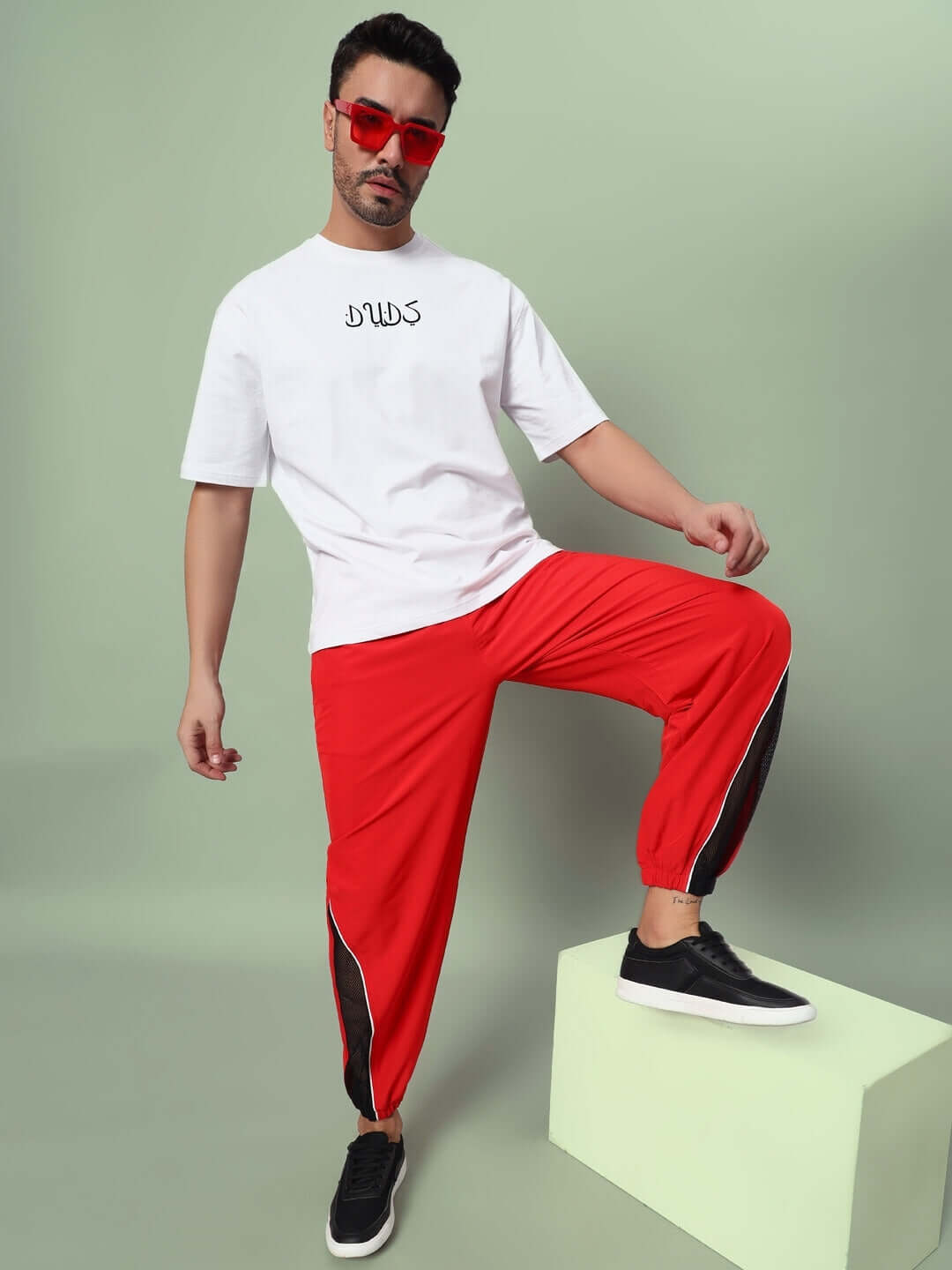 Man wearing PLEXUS JOGGERS in red, styled with a white DUDS shirt and sunglasses, showcasing modern tailored fashion.