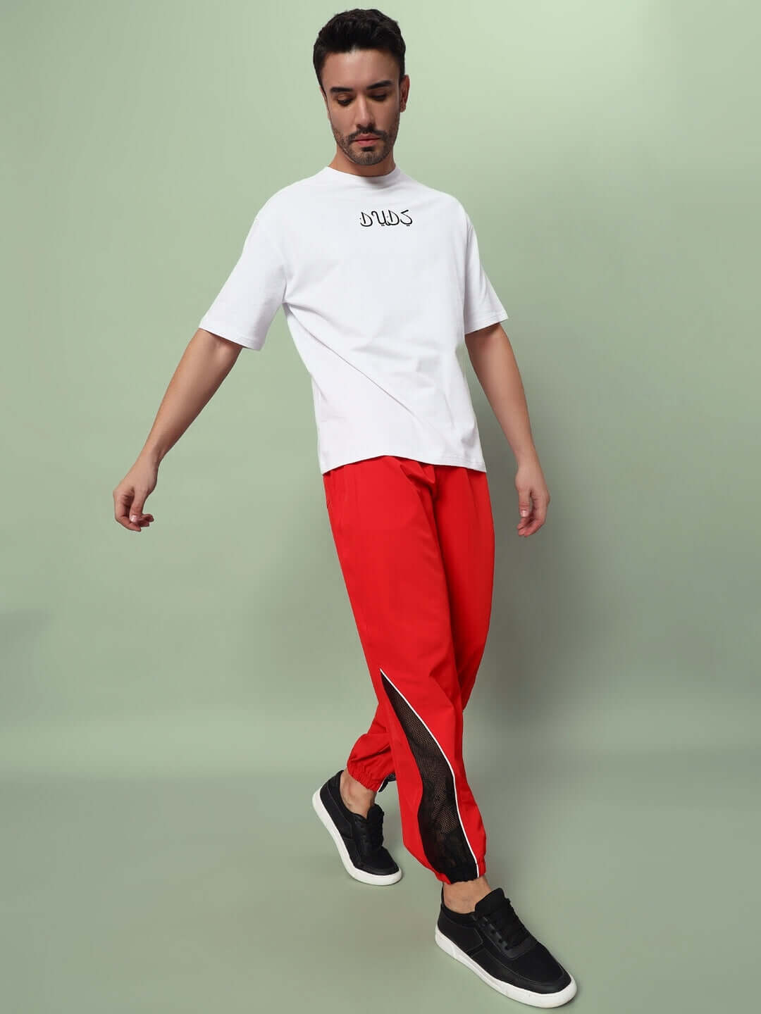 Man wearing PLEXUS JOGGERS in red, paired with a white t-shirt and black shoes, showcasing comfortable and stylish casual wear.