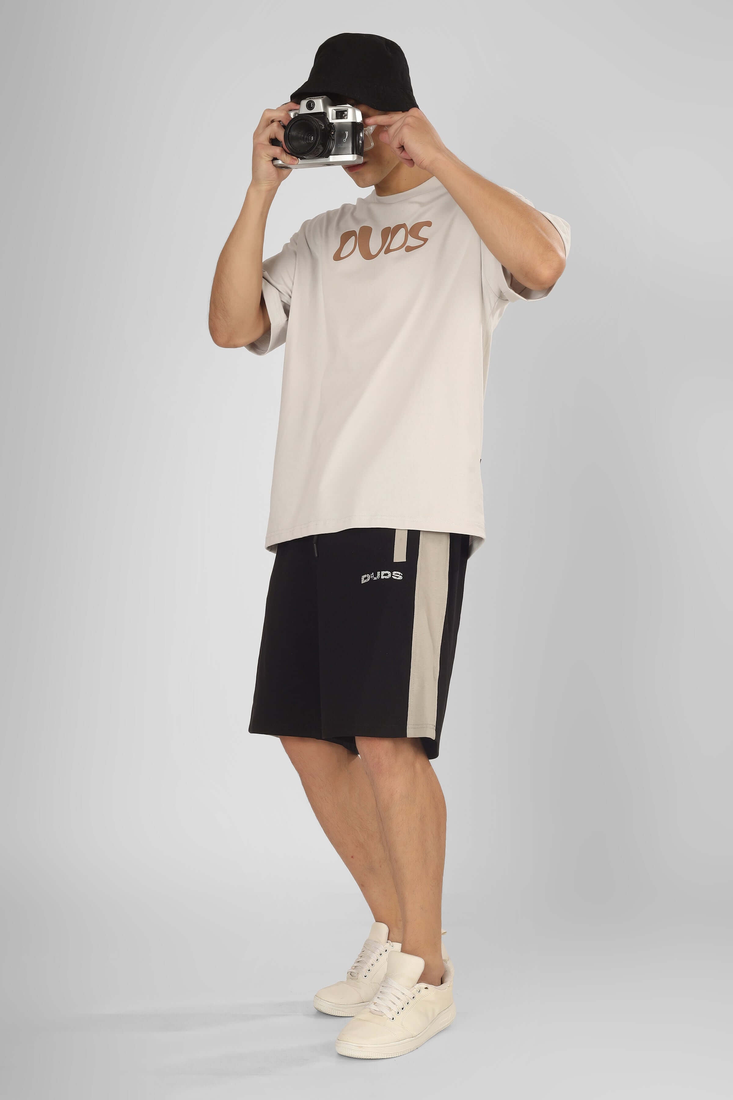Model wearing PLUTO Contrast Regular Fit Black Shorts with DUDS t-shirt, holding a camera. Custom Fit available for prepaid orders.