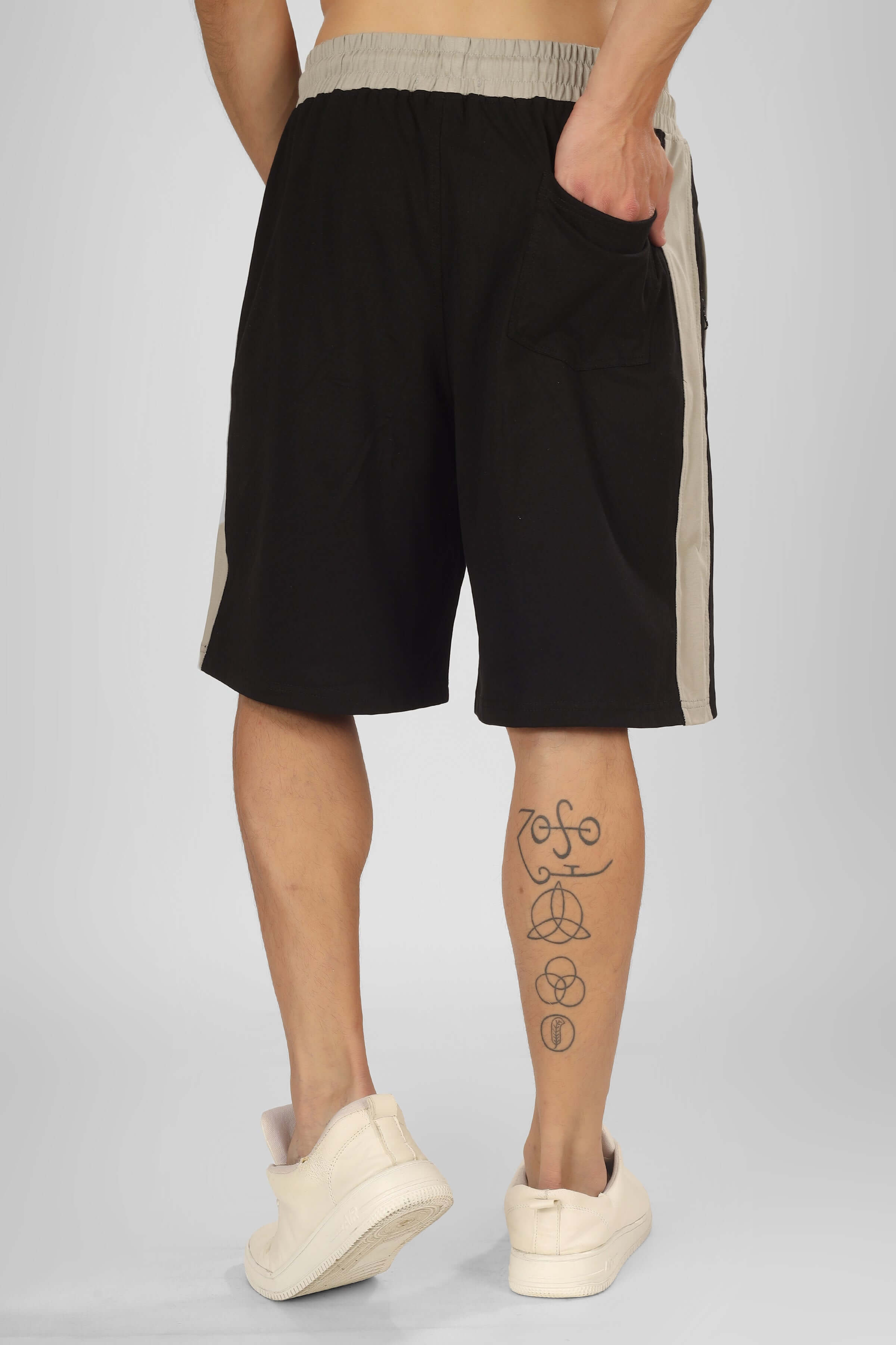 Back view of black PLUTO CONTRAST REGULAR FIT SHORTS featuring side panel, worn by a model with tattoos and white sneakers.