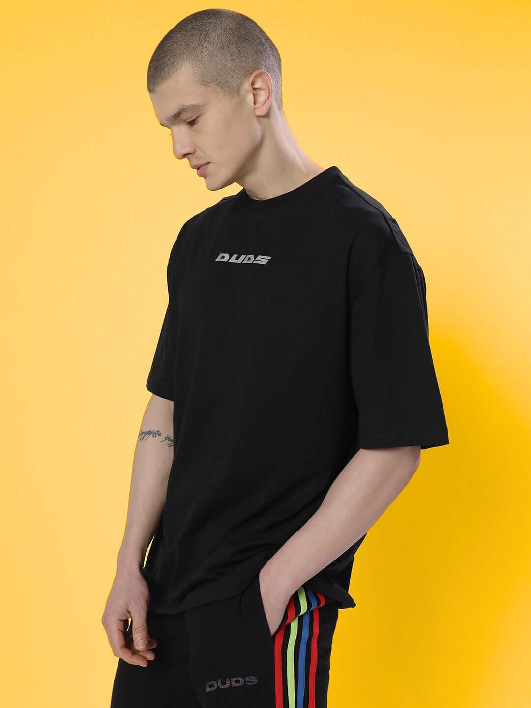 Model wearing black oversized T-shirt with subtle logo, featuring premium cotton blend fabric, against a bright yellow background.
