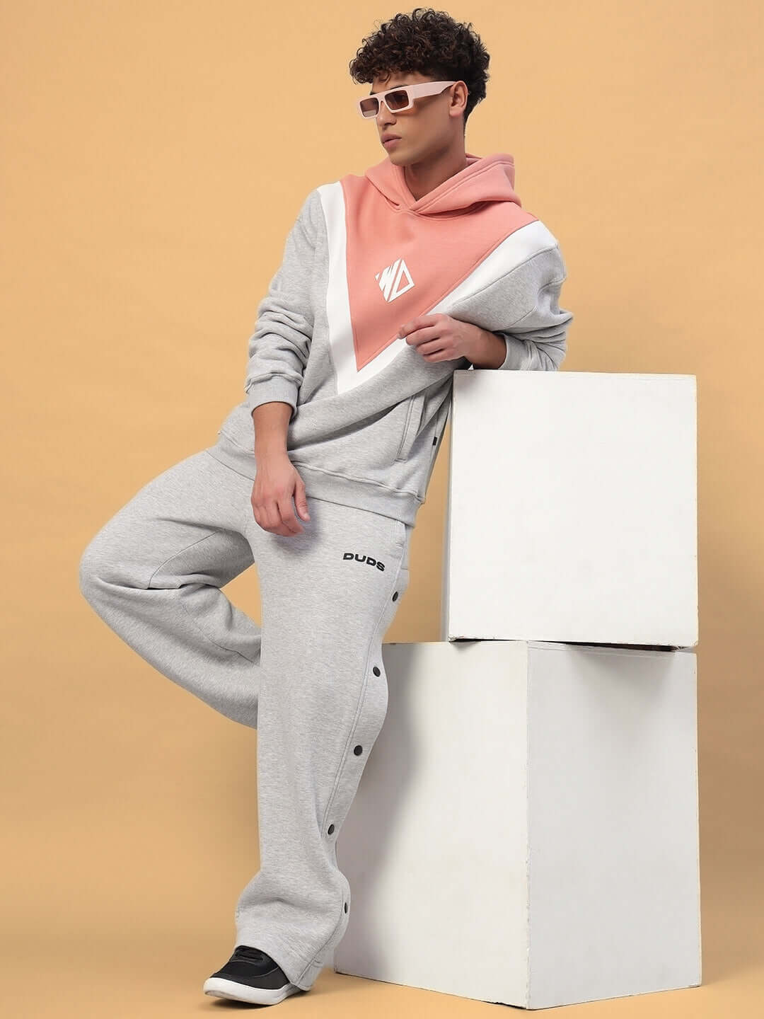 Man wearing POLAR FLEECE COLORBLOCK CO-ORD GREY PEACH hoodie and joggers, stylish streetwear set against beige background.