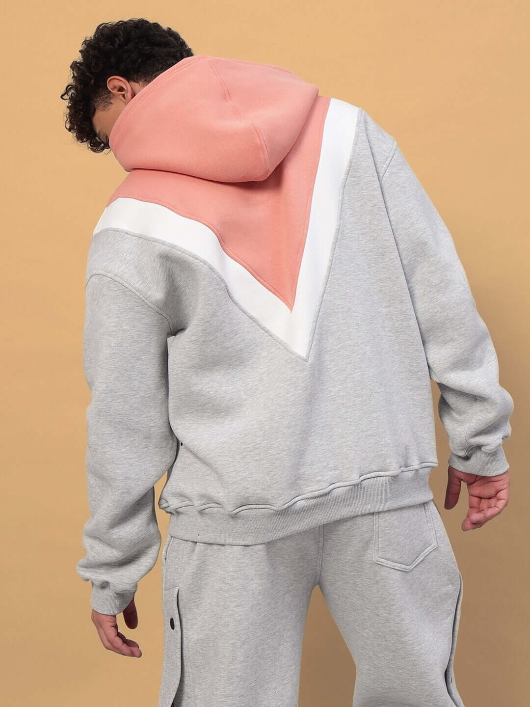 Back view of a model wearing a POLAR FLEECE COLORBLOCK HOODIE GREY PEACH with peach and grey panels, showcasing streetwear style.