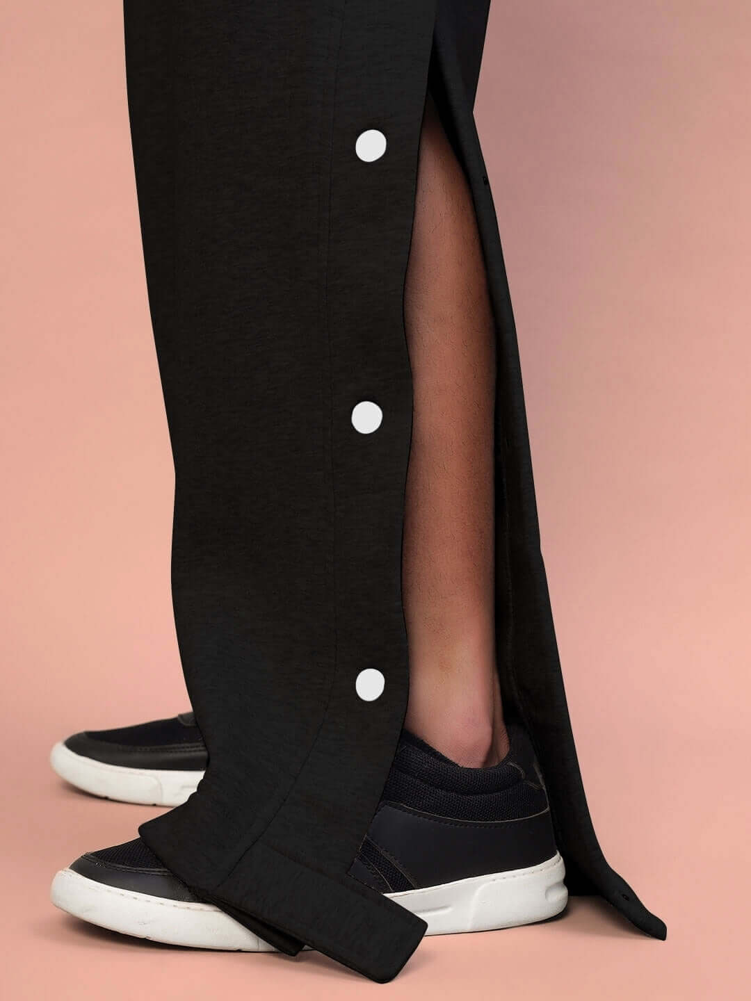 Close-up of POLAR cotton fleece jogger in black with side buttons, worn with black sneakers against a peach background.