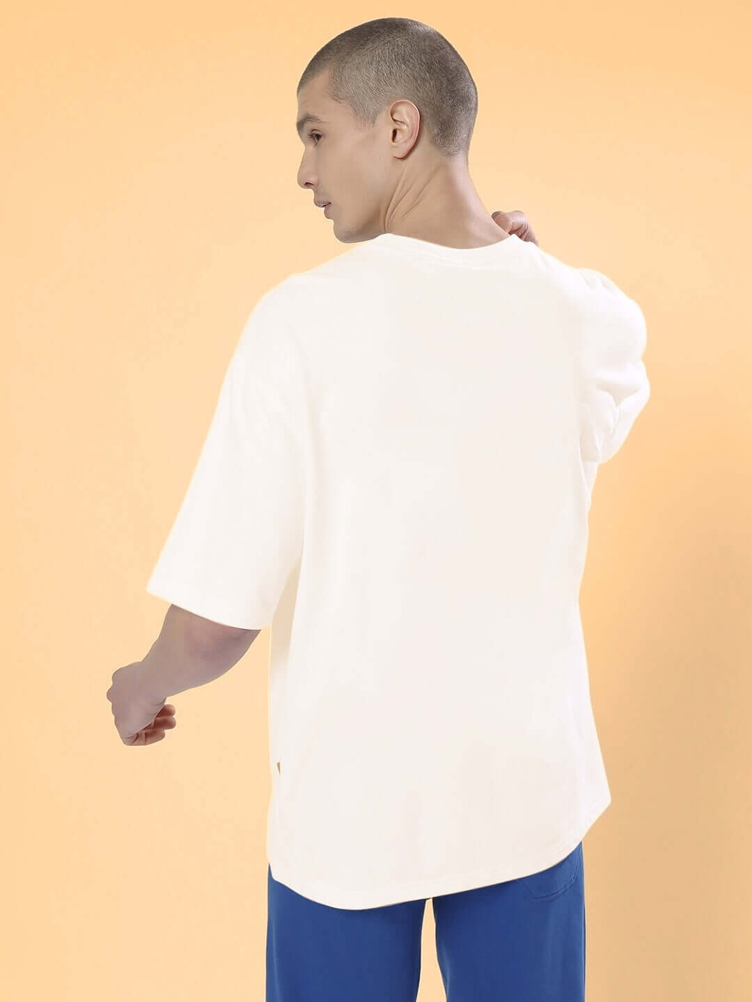 Back view of model wearing POPEYE over-sized cream t-shirt with blue pants, showcasing casual and relaxed style.