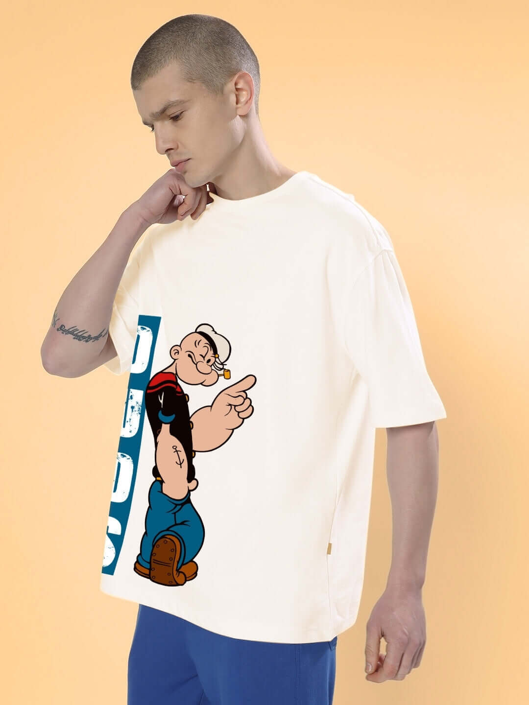 Man wearing cream oversized Popeye t-shirt from DUDS, featuring customization options, with orange background.