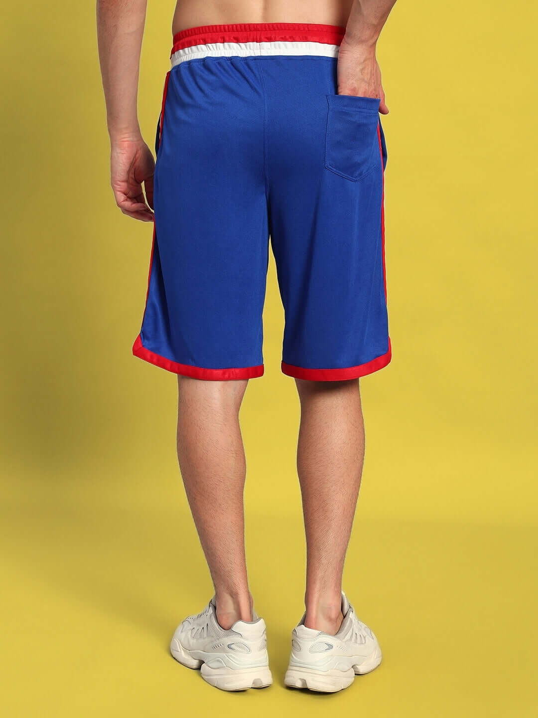Back view of a person wearing PORTIA REGULAR FIT SHORTS ROYAL BLUE with red trim in a casual setting.
