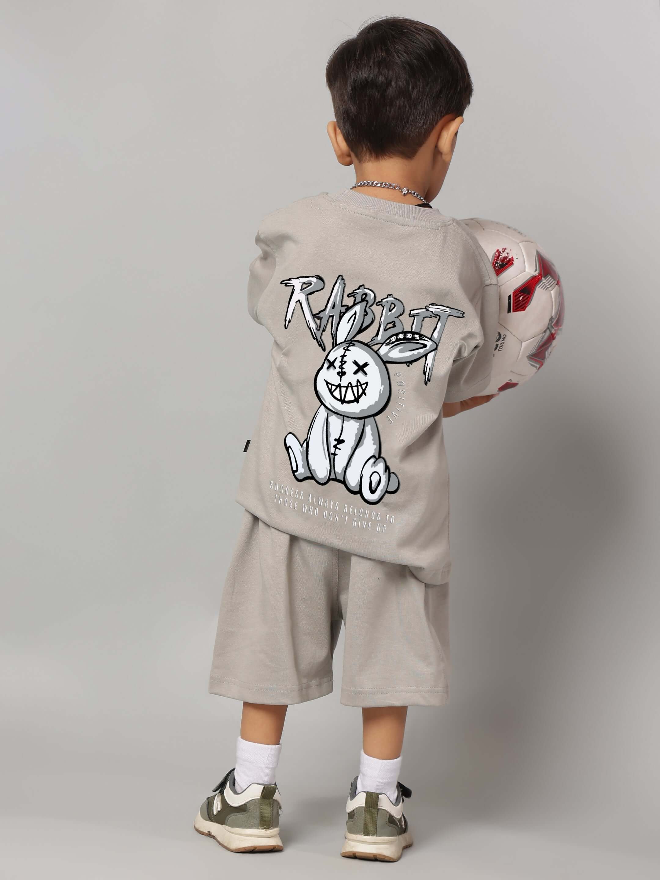 Young boy wearing grey Positive Rabbit kids co-ord set, holding a soccer ball, showcasing playful rabbit design on the back.