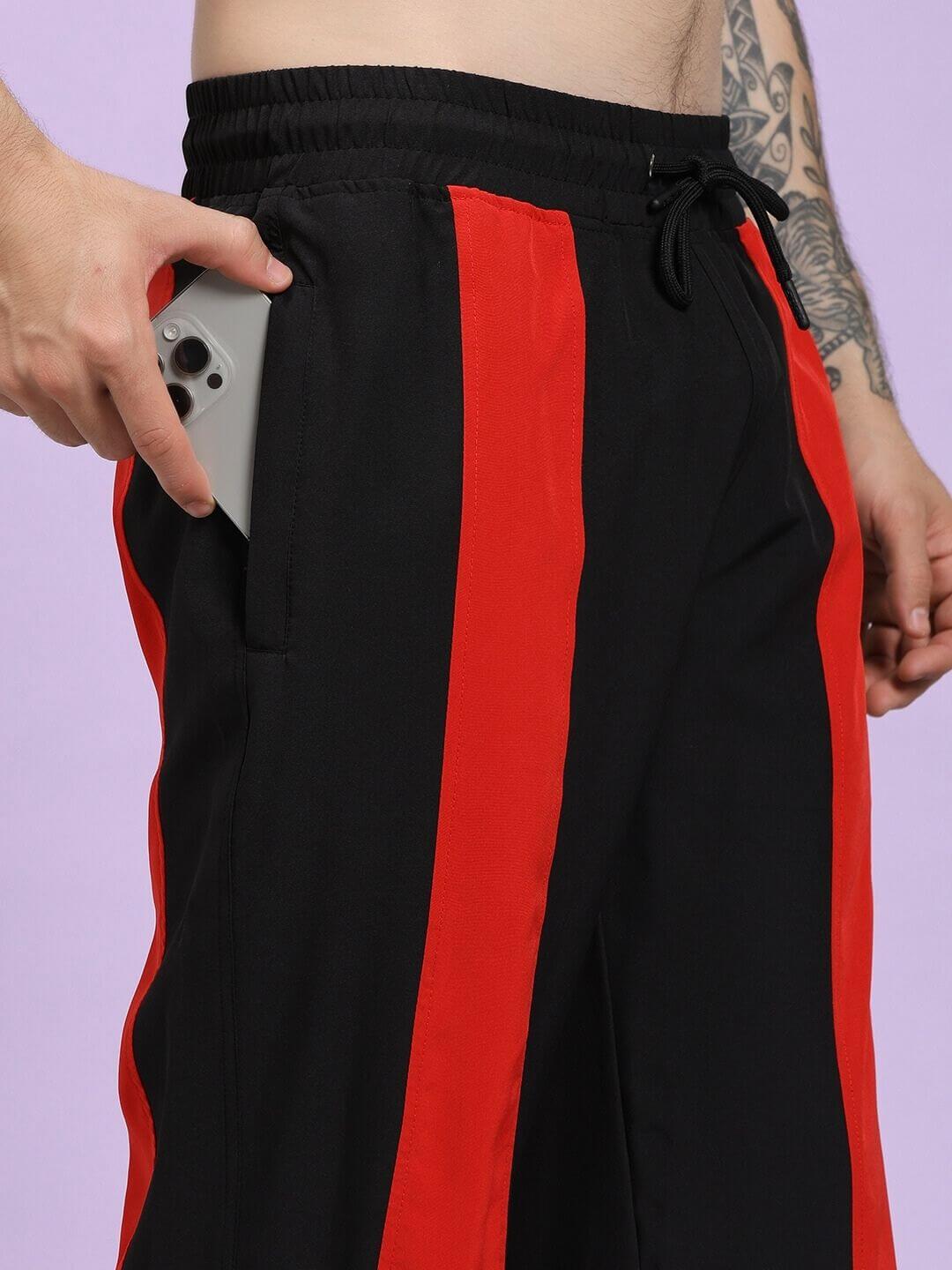 POWER BLOCK RELAXED FIT JOGGER BLACK RED Black and red striped pants with a person holding a phone on a light purple background