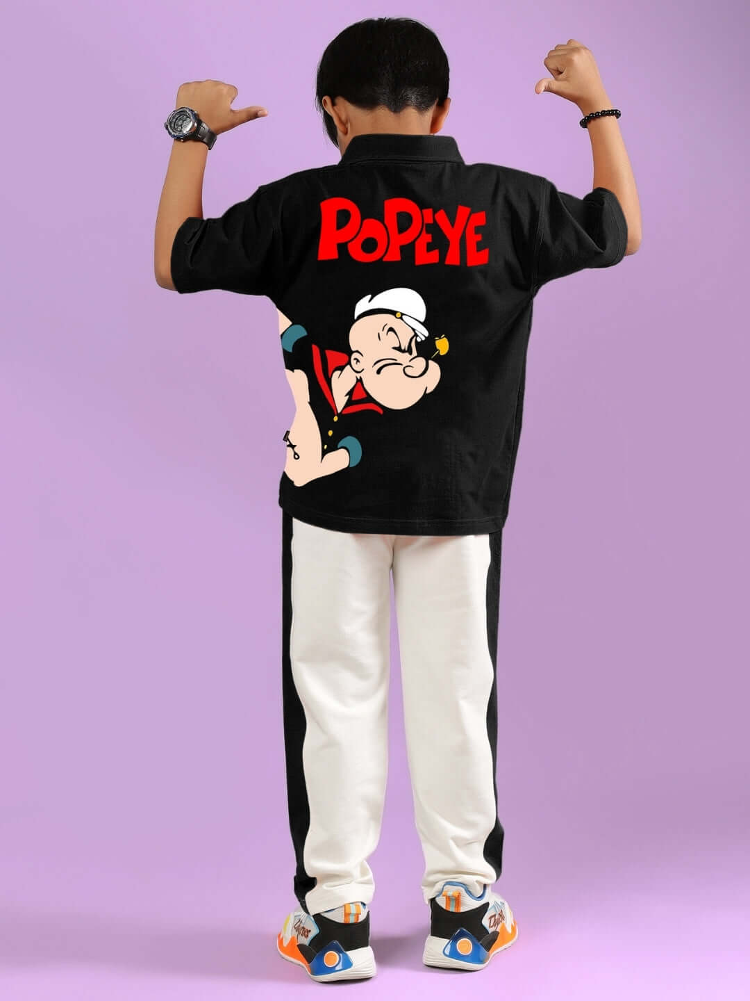Child wearing a black and off-white Popeye-themed coordinated outfit, featuring a cartoon character on the back, against a purple background.
