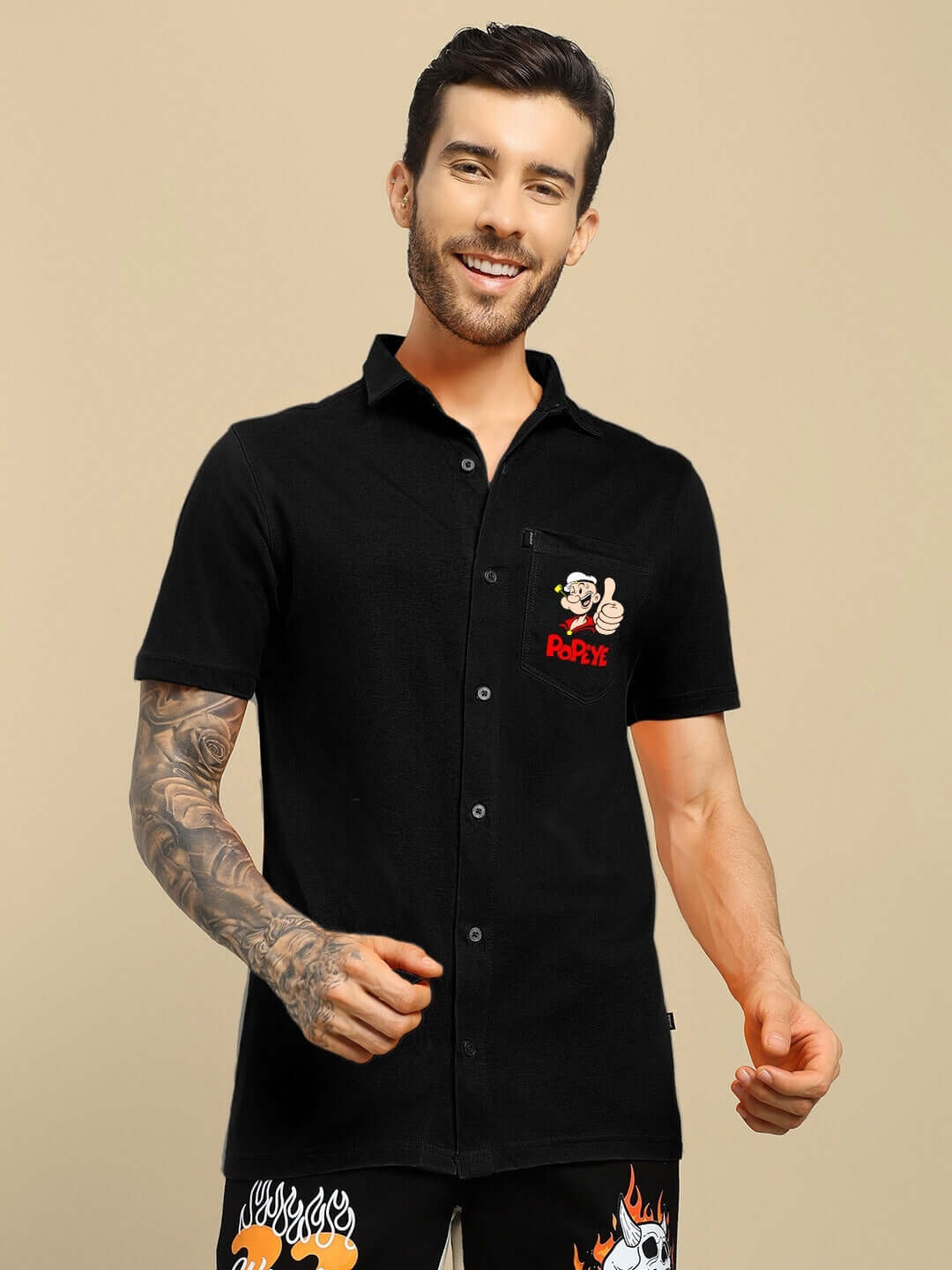 Man wearing a black POWER MEN Popeye printed shirt, featuring a casual design, showcasing a cartoon image and logo on the pocket.