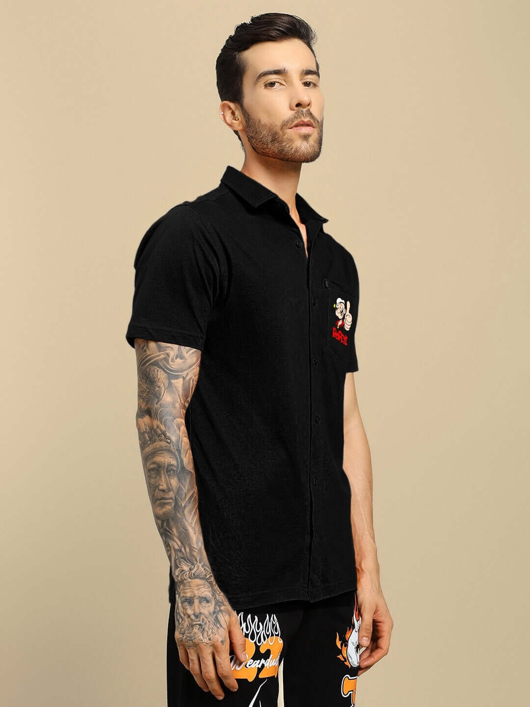 Model wearing a black POWER MEN Popeye printed shirt with tattooed arm, showcasing unique design and style by DUDS.